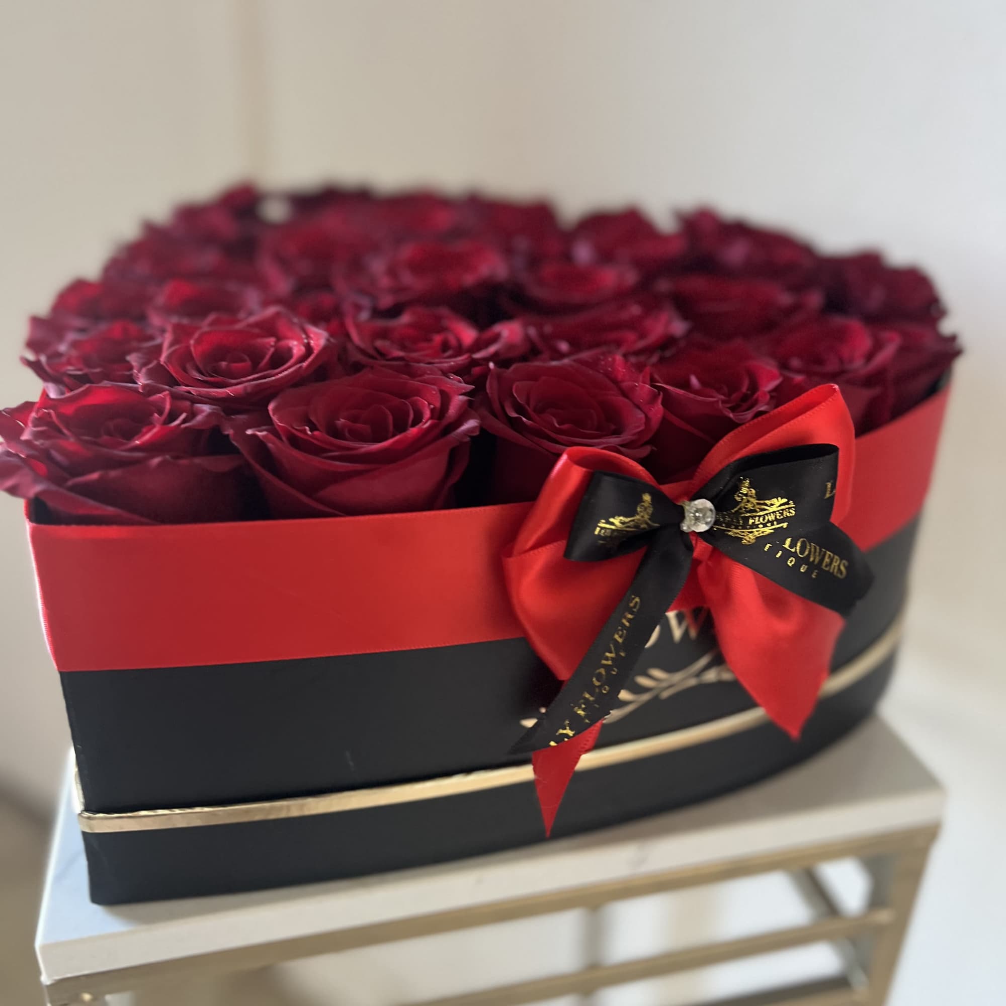 Boxed arrangement of deep red roses with a red and black ribbon bow