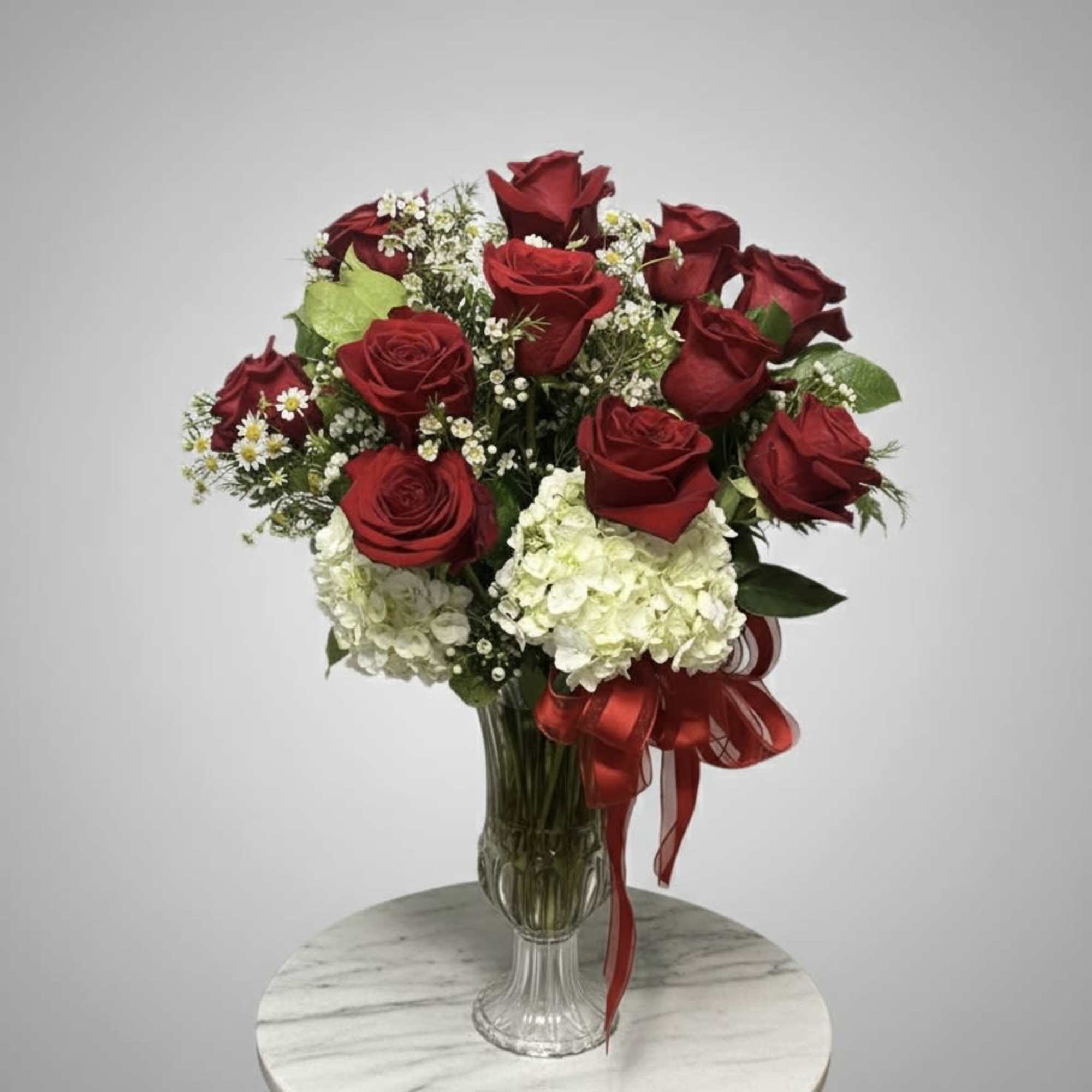 Red roses and white hydrangeas in a clear glass vase with a red ribbon