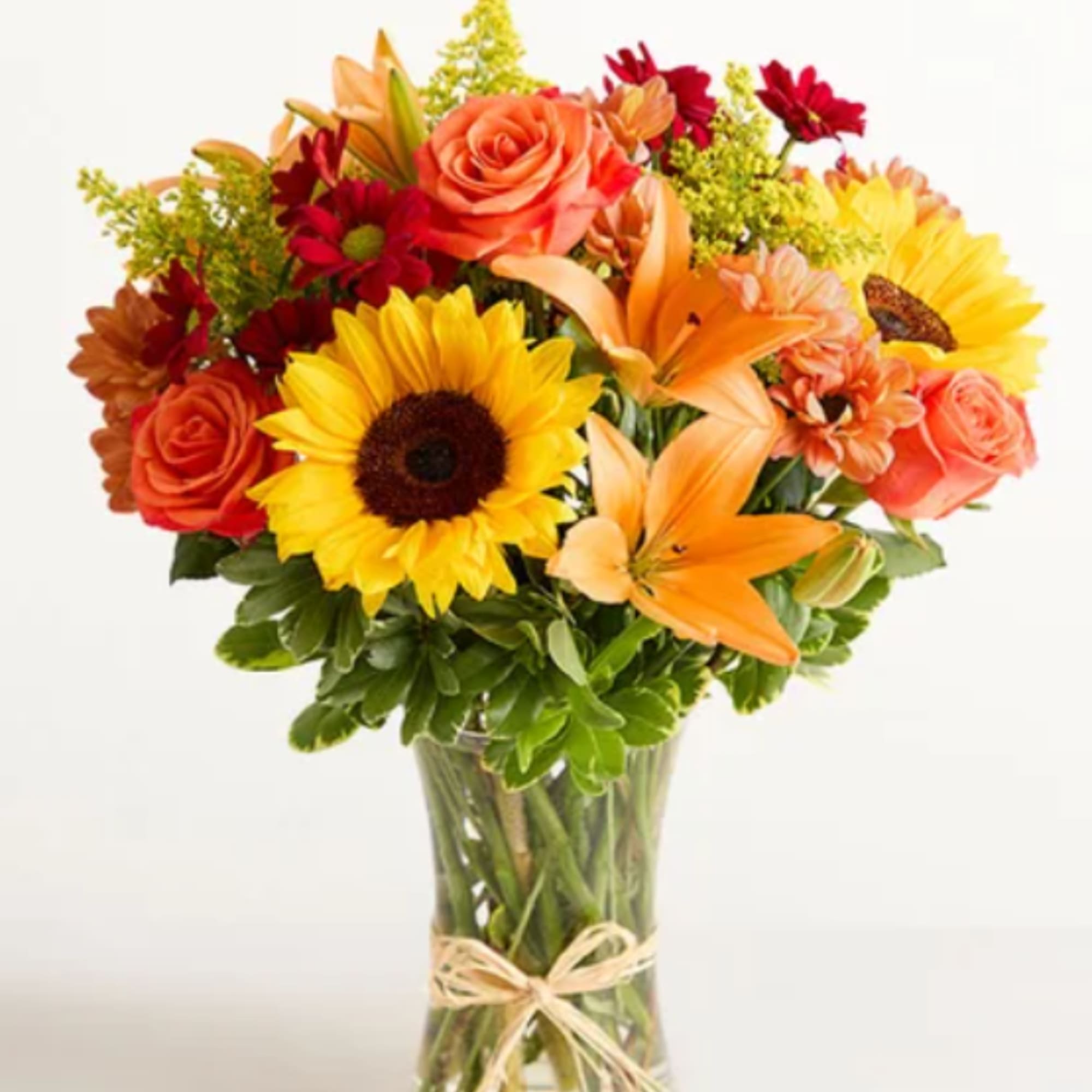Bouquet of sunflowers, orange roses, and lilies in a glass vase
