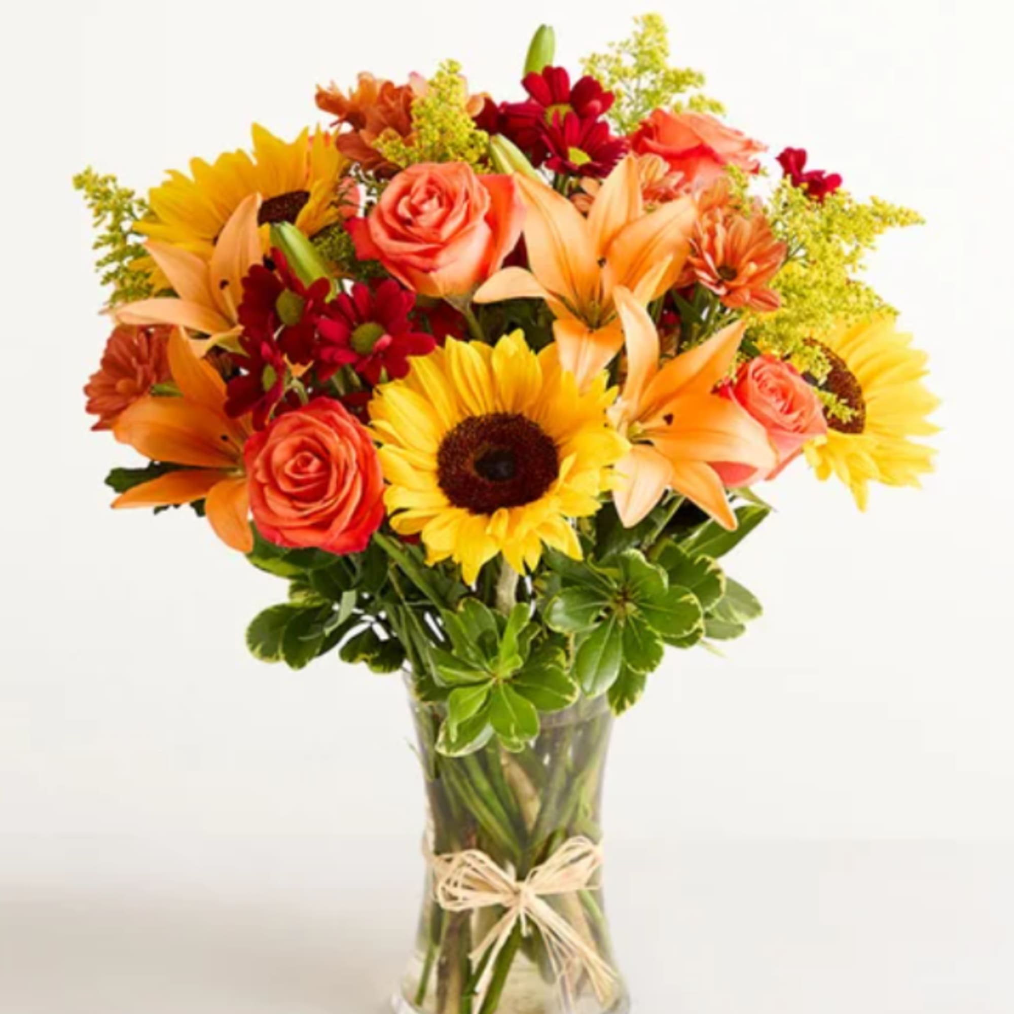 Bouquet of sunflowers, roses, lilies, and daisies in a clear glass vase