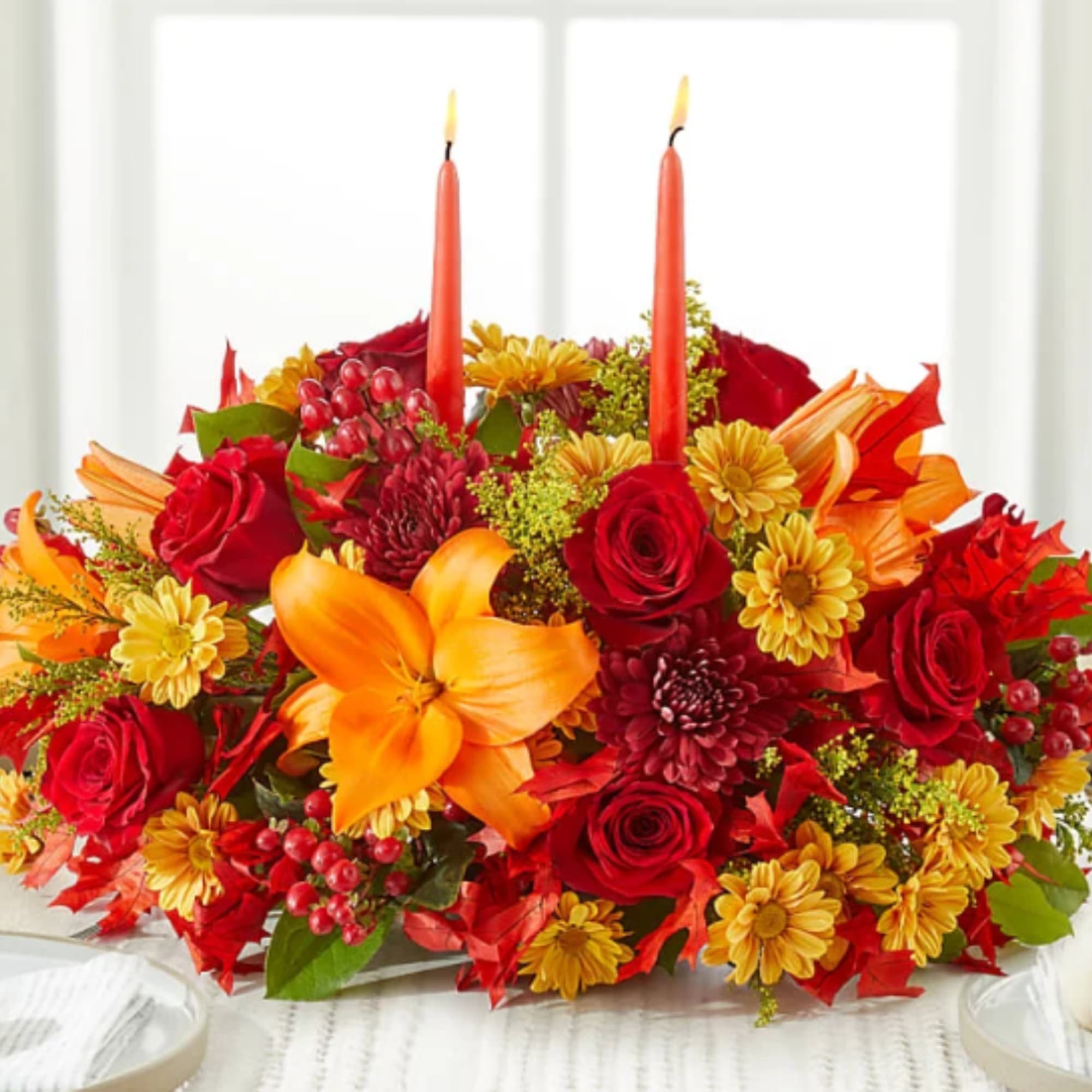 Red and orange floral centerpiece with two lit taper candles