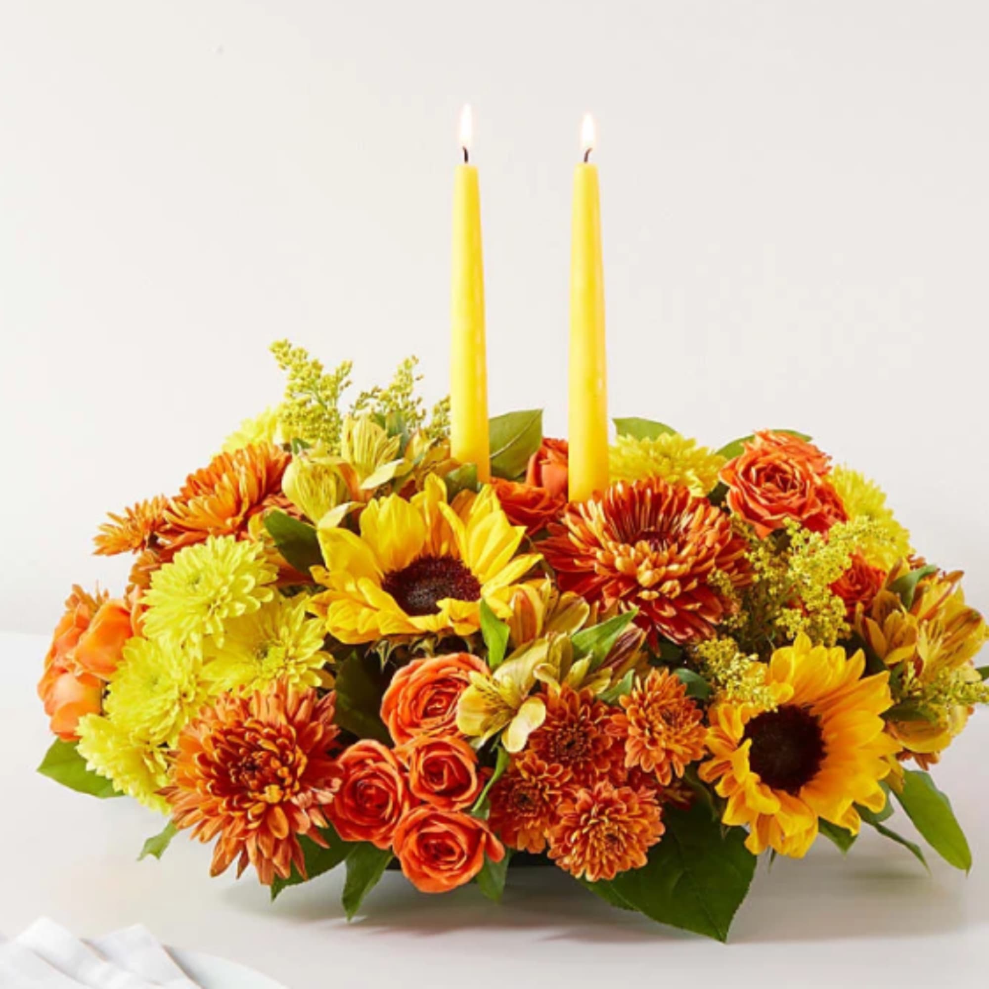 Orange and yellow flower arrangement with two lit taper candles