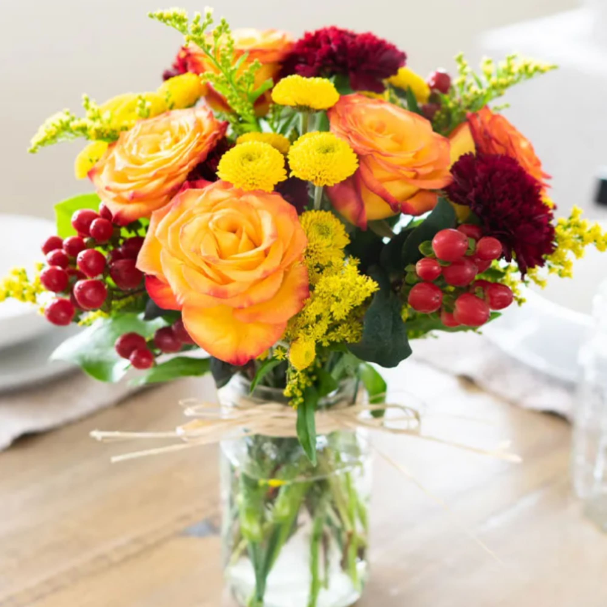 Bouquet of orange roses and yellow flowers in a clear glass vase