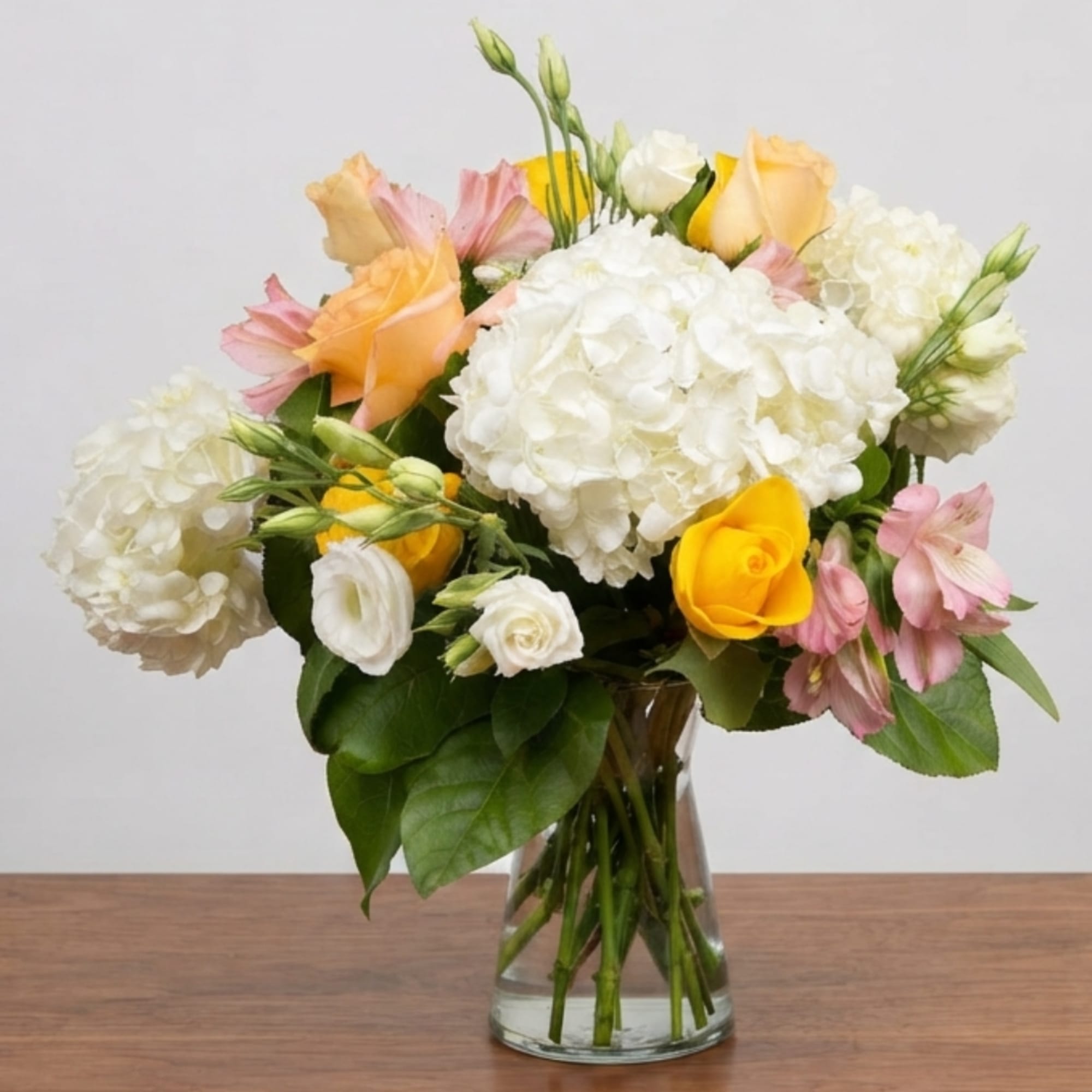 Mixed bouquet of white hydrangeas, yellow roses, and pink alstroemeria in a glass vase