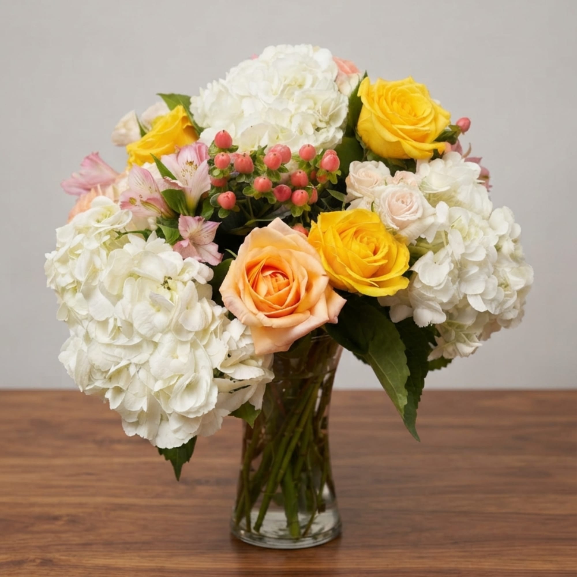Mixed bouquet of white hydrangeas, yellow and peach roses in a glass vase