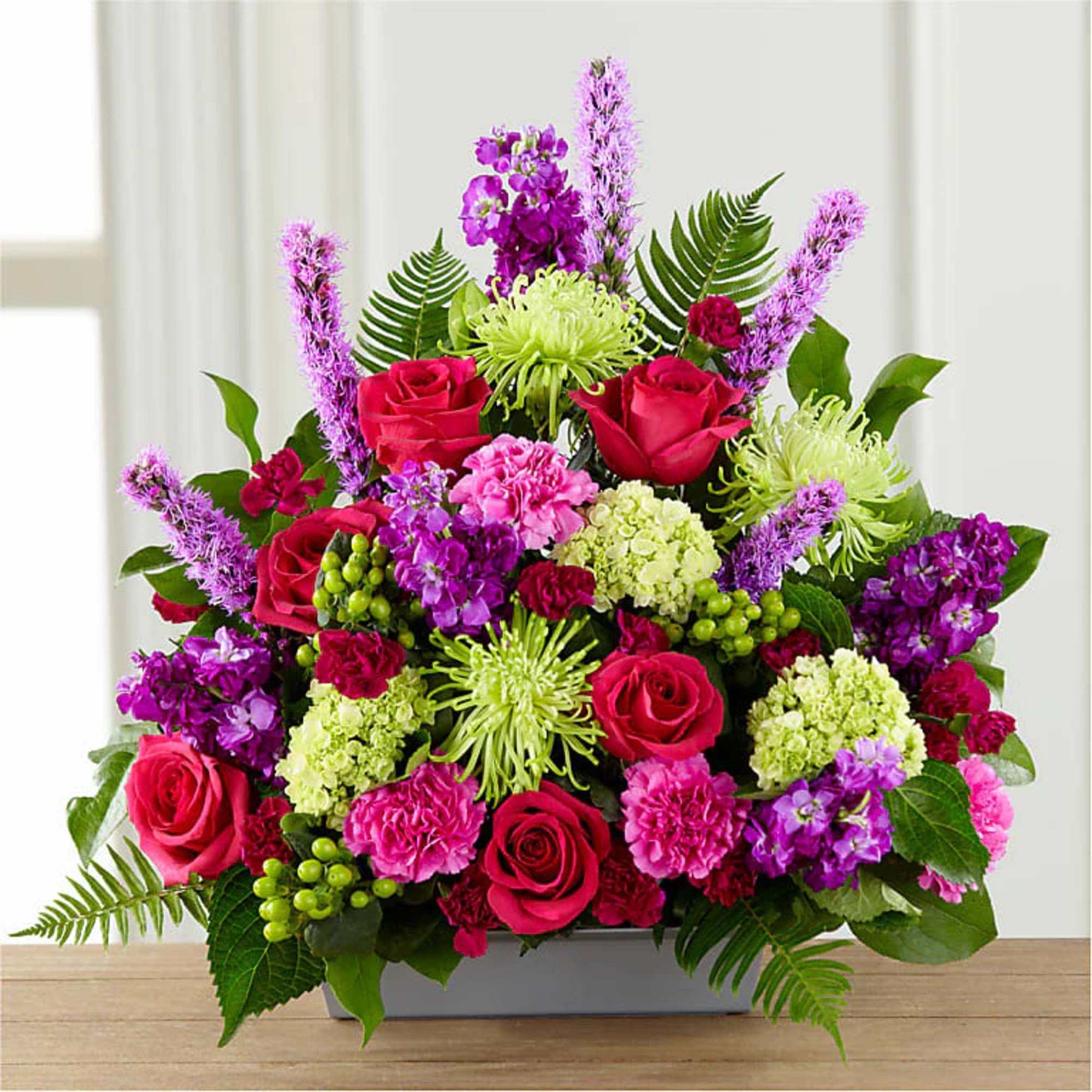 Mixed bouquet of roses, chrysanthemums, and purple blooms in a low rectangular container