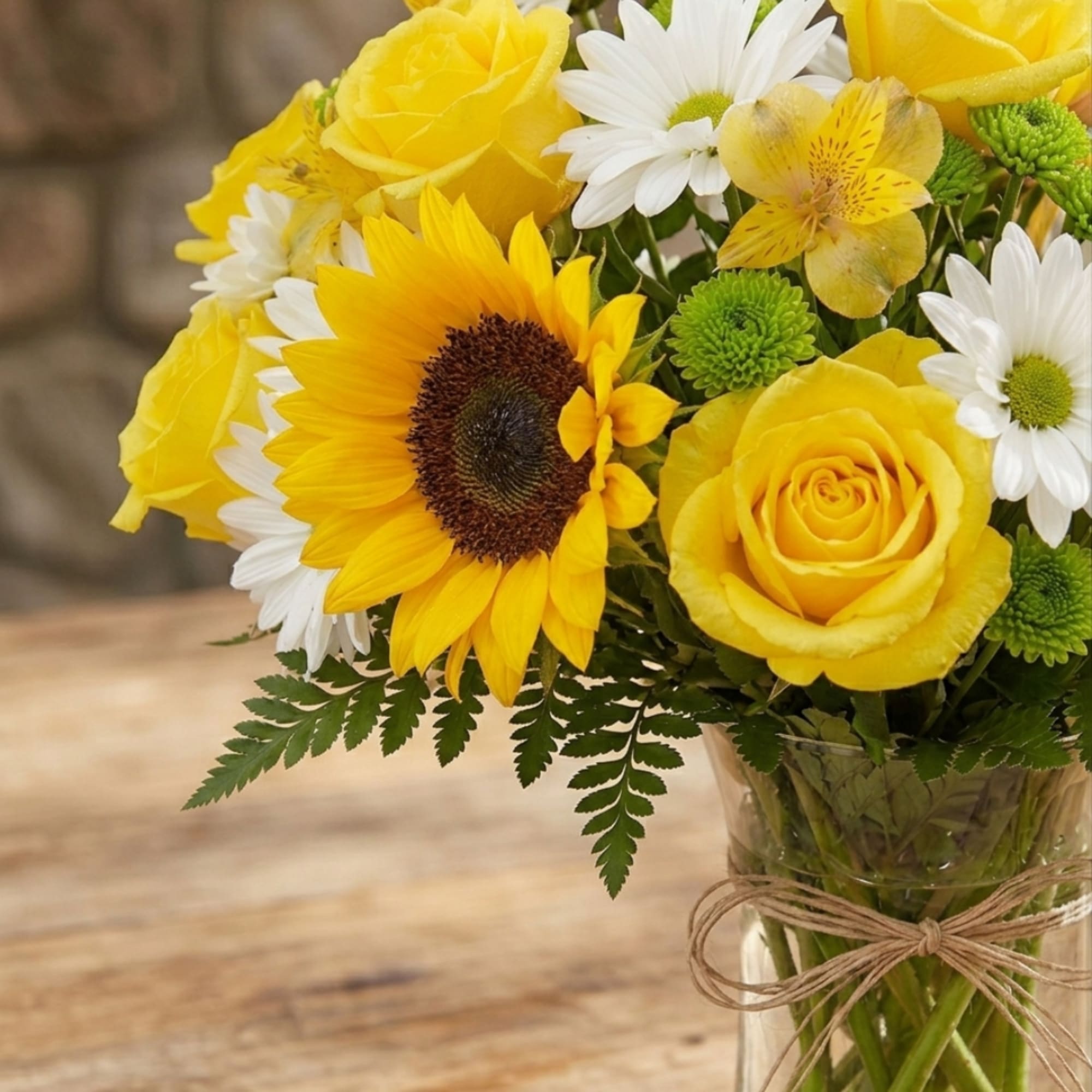Yellow roses and a sunflower in a glass vase with white daisies