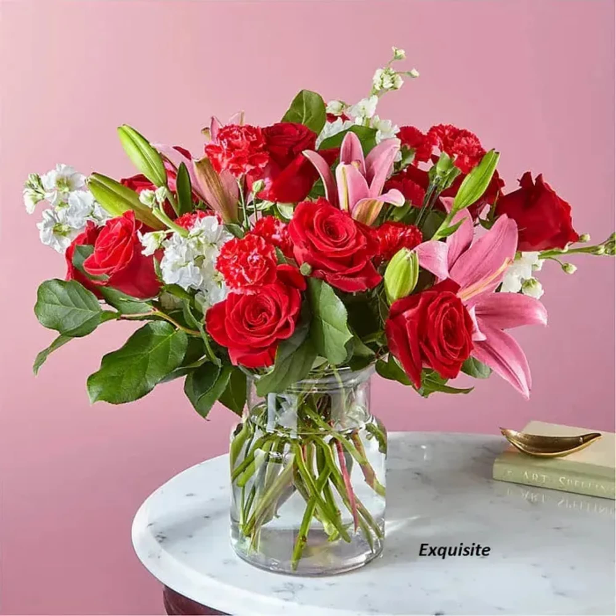 Bouquet of red roses, pink lilies, and white filler flowers in a glass vase