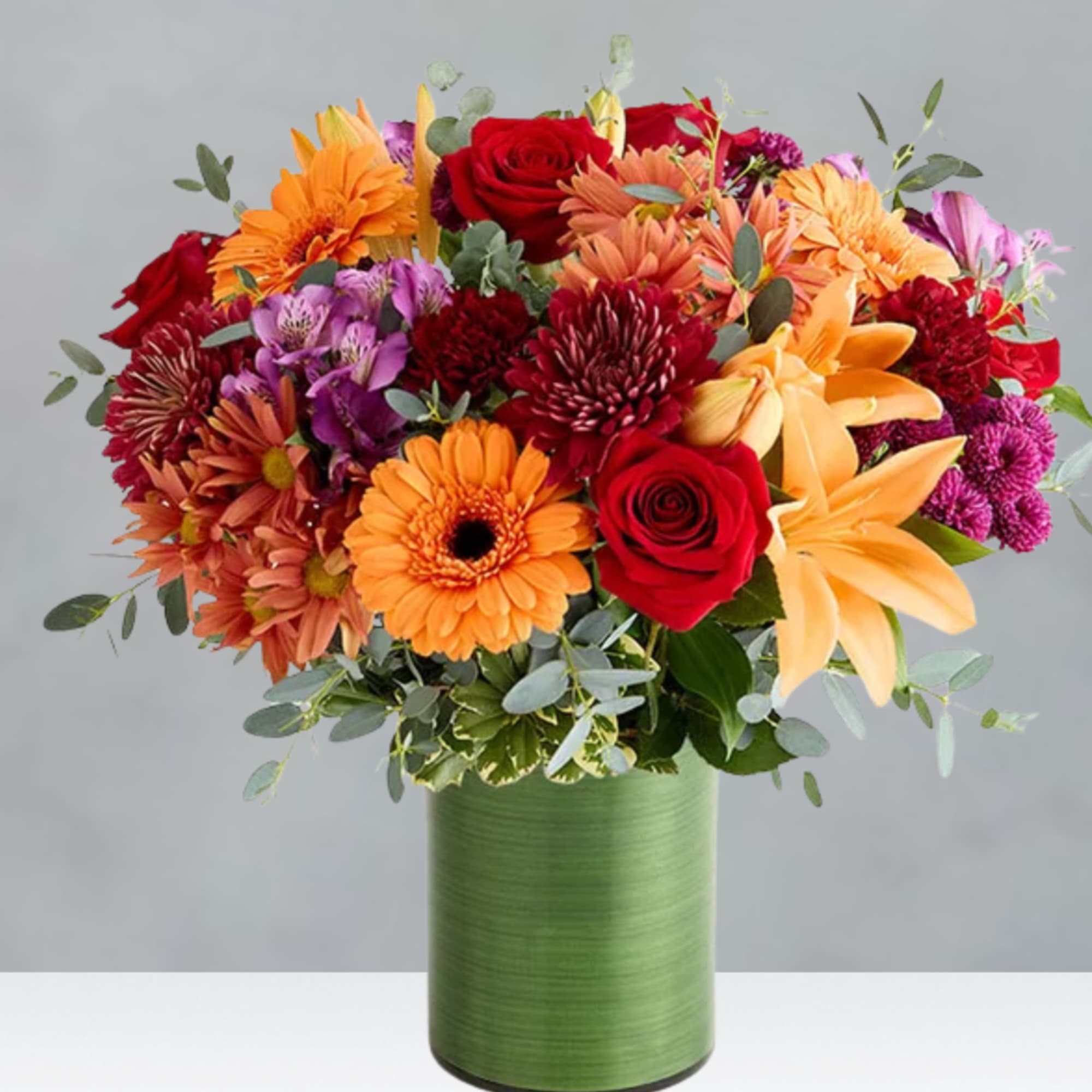 Mixed bouquet of red, orange, and purple flowers in a green vase
