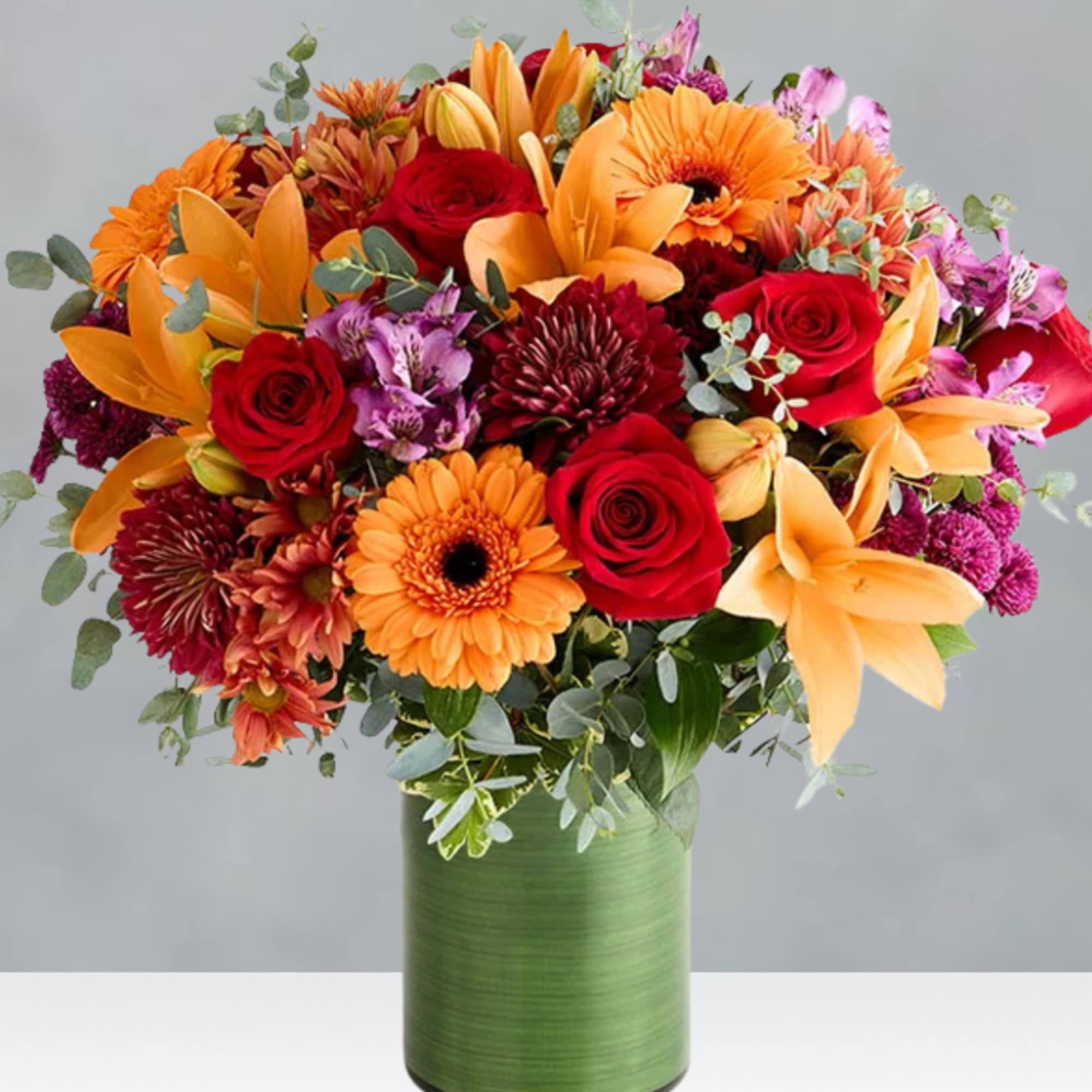 Bouquet of orange lilies, red roses, and gerbera daisies in a green vase