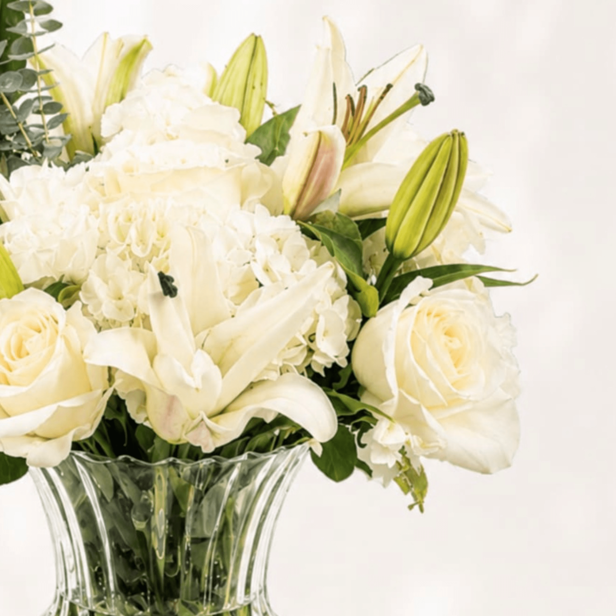 White floral arrangement in a clear glass vase with roses and lilies