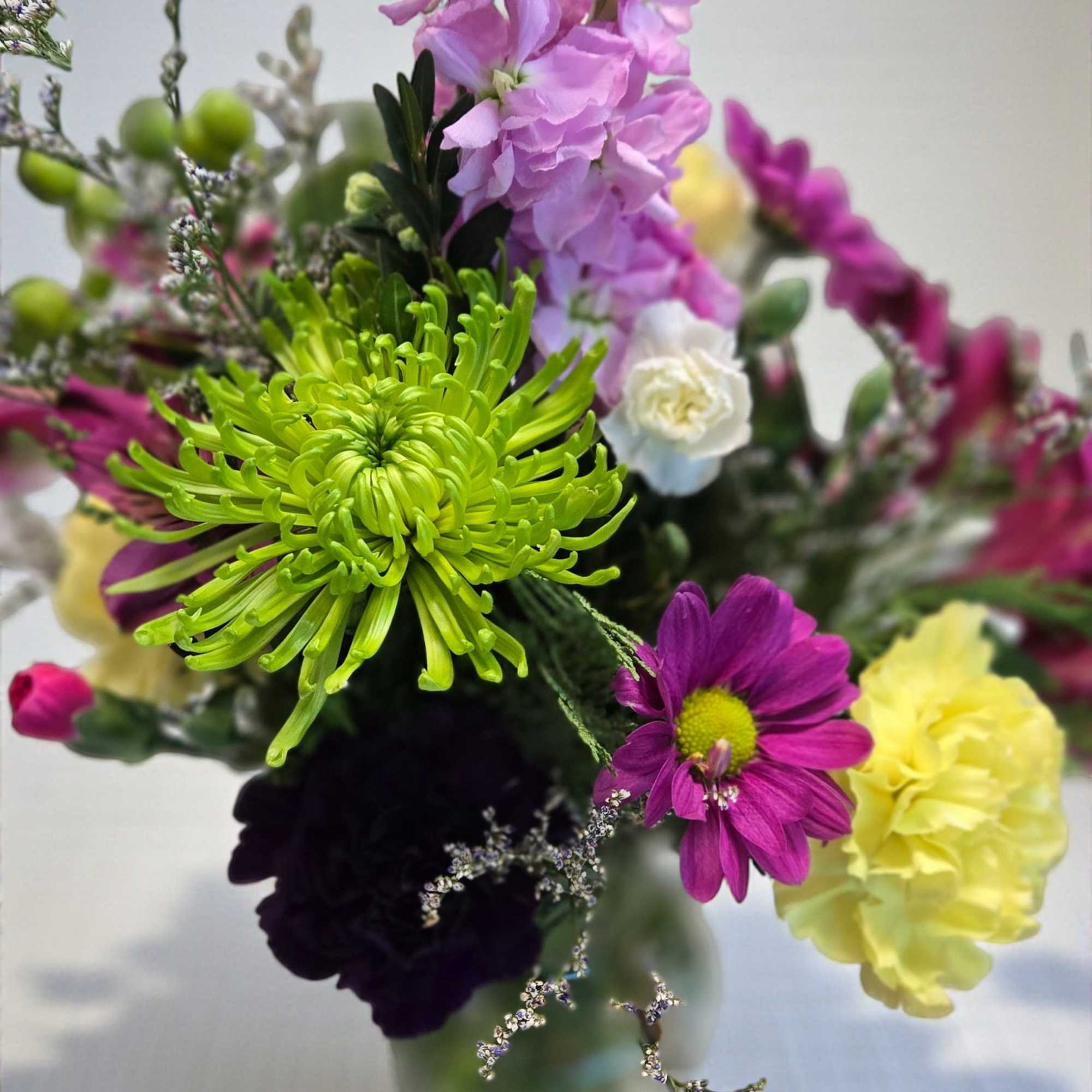 Mixed bouquet of pink, purple, yellow, and green flowers in a glass vase