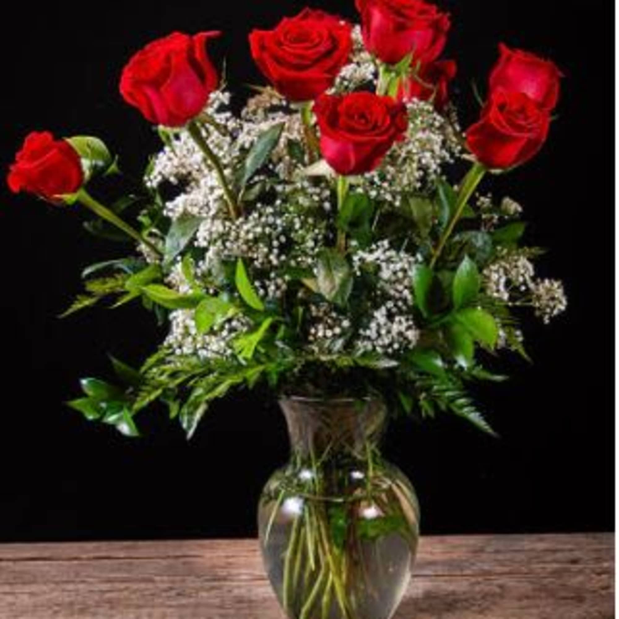 Red roses arranged in a clear glass vase with white filler flowers