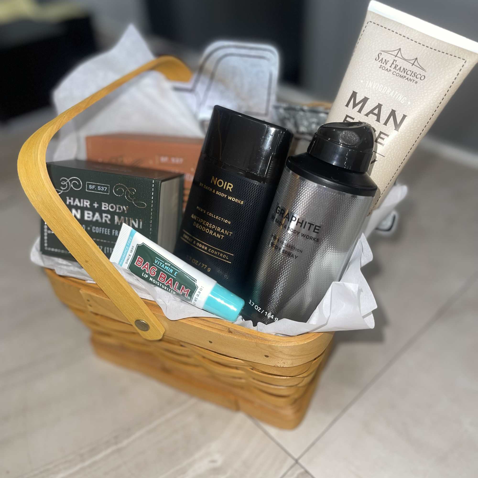 Basket of men’s grooming products with soap, deodorant, body spray, and lip balm