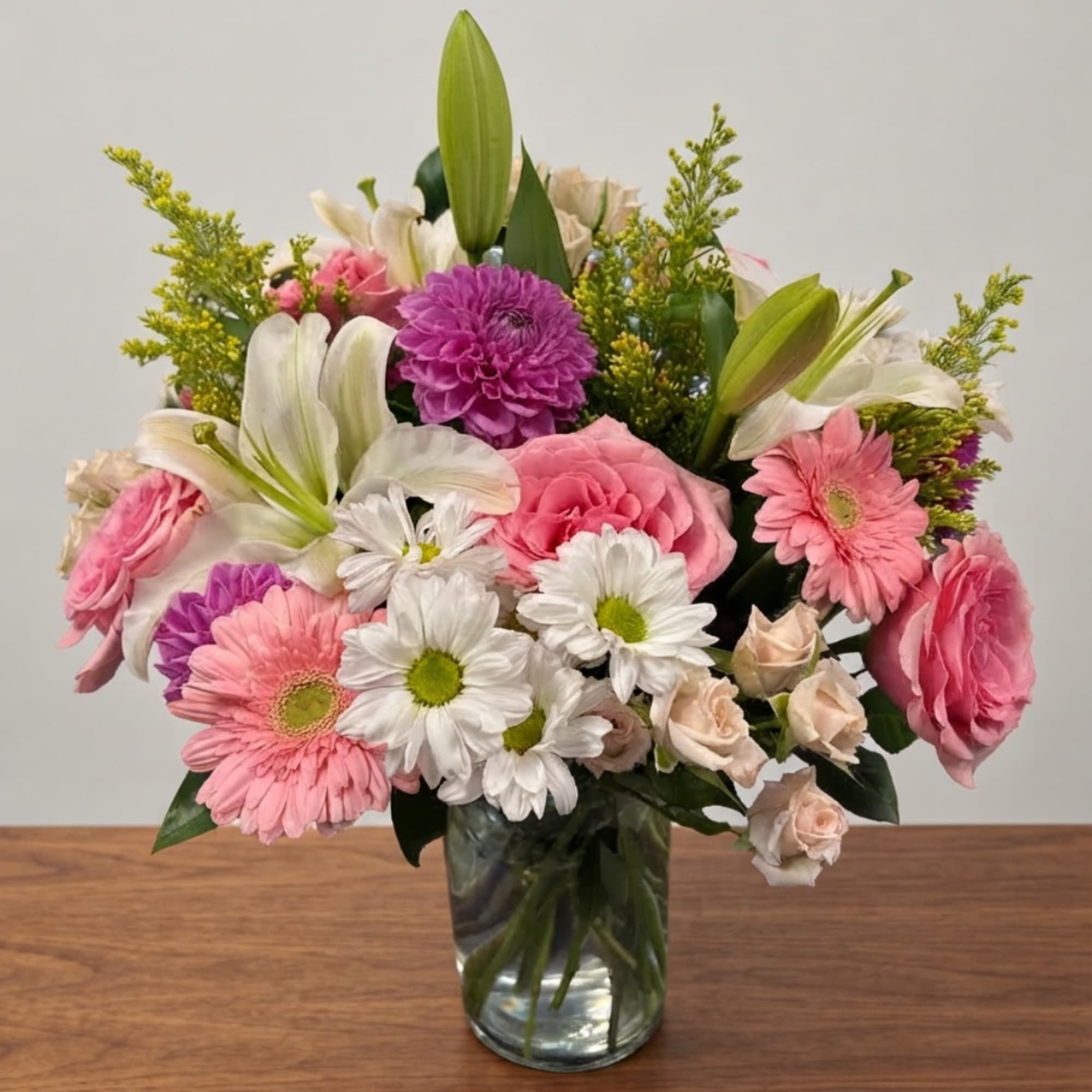 Mixed pink, white, and purple flowers arranged in a clear glass vase