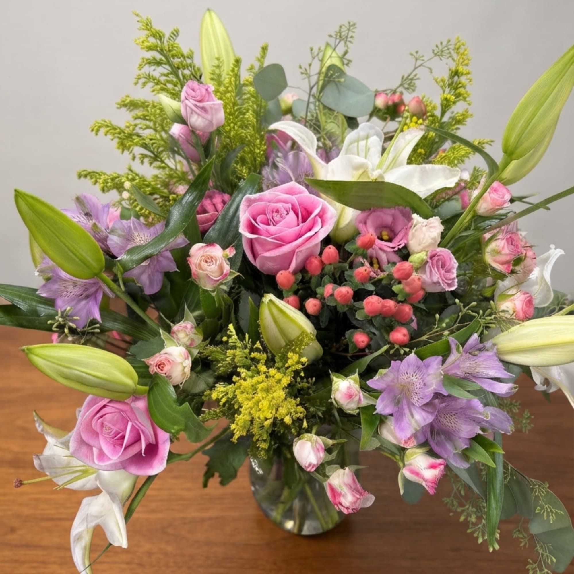 Pink roses and white lilies in a glass vase with purple flowers