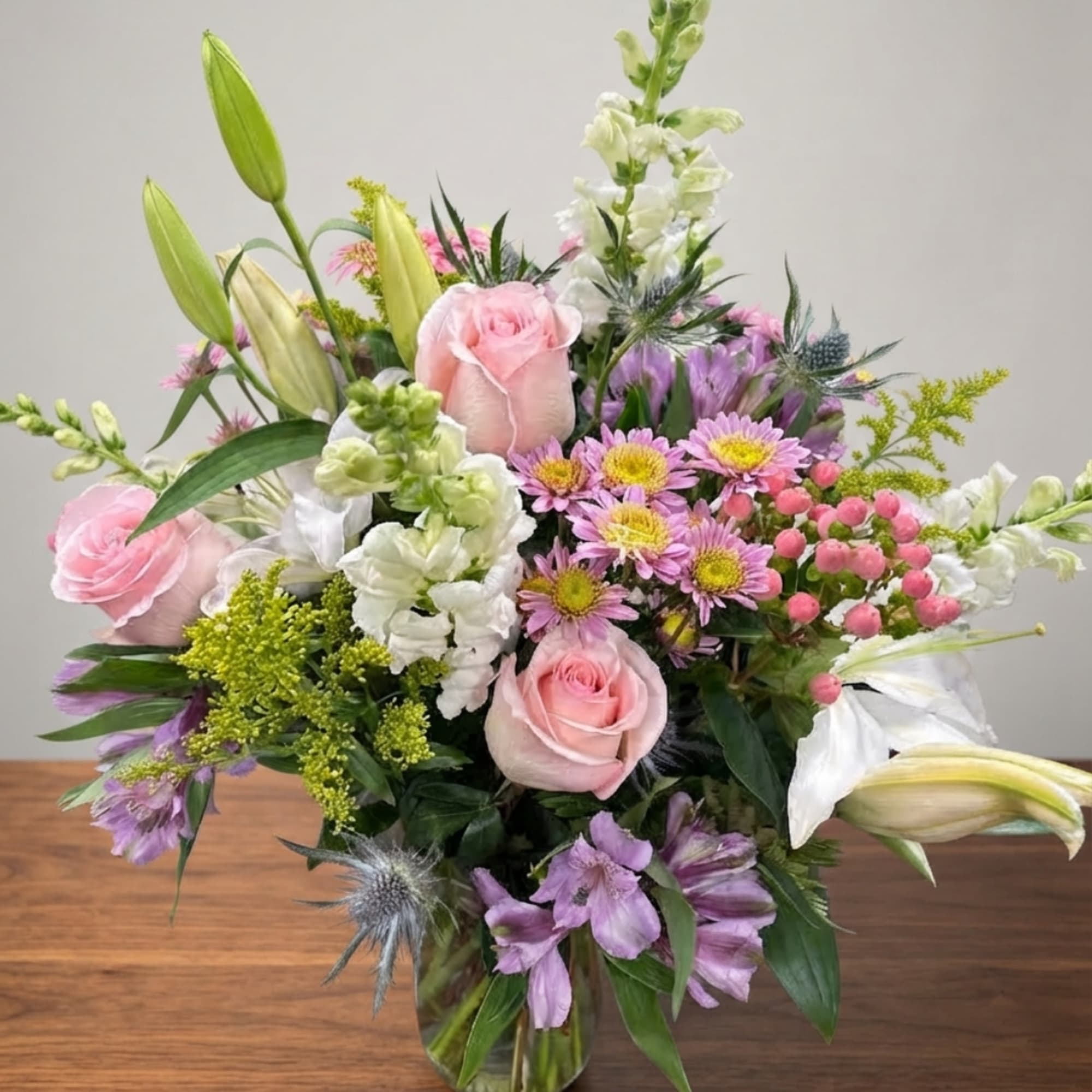 Mixed bouquet of pink roses, white lilies, and purple flowers in a glass vase
