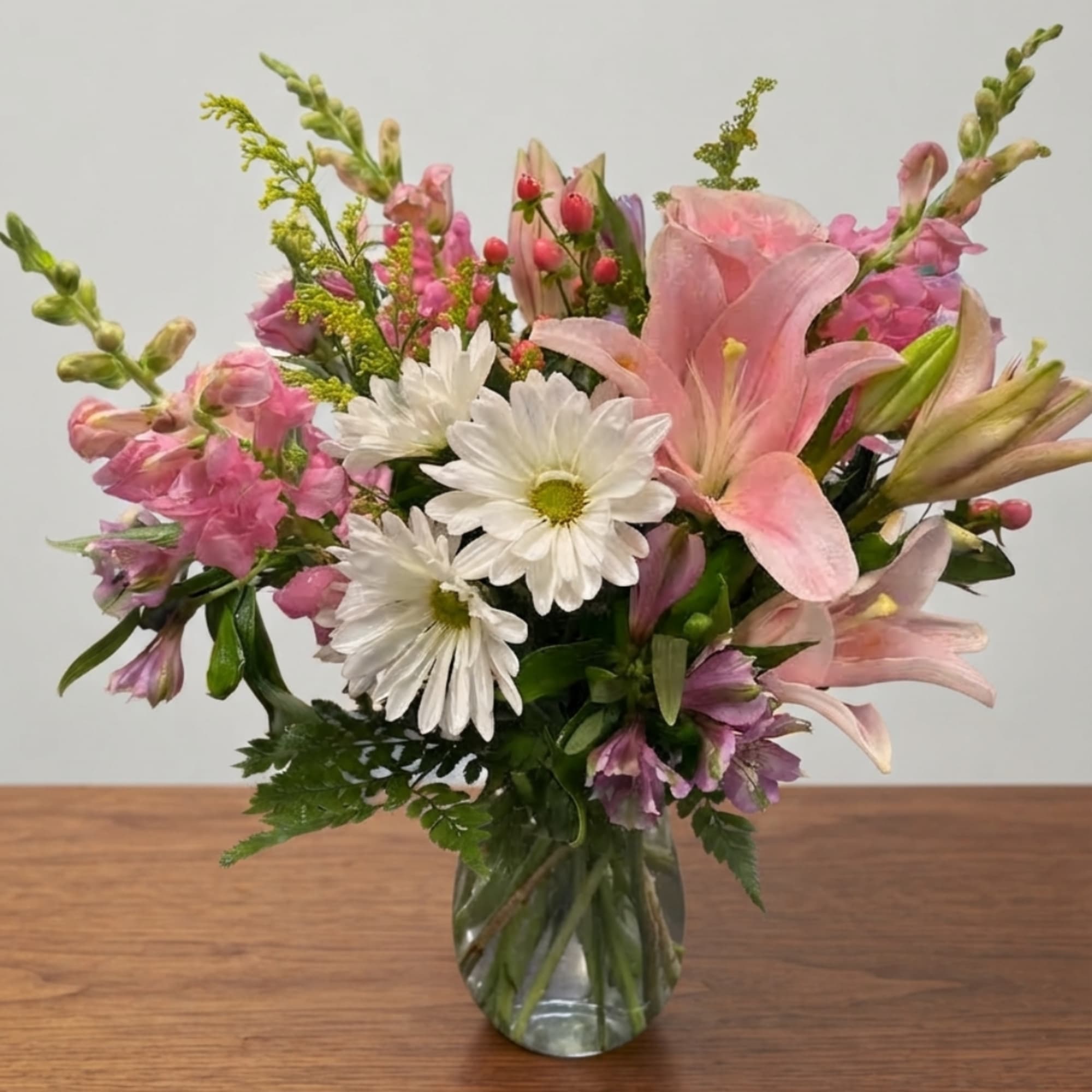 Pink lilies and white daisies arranged in a clear glass vase