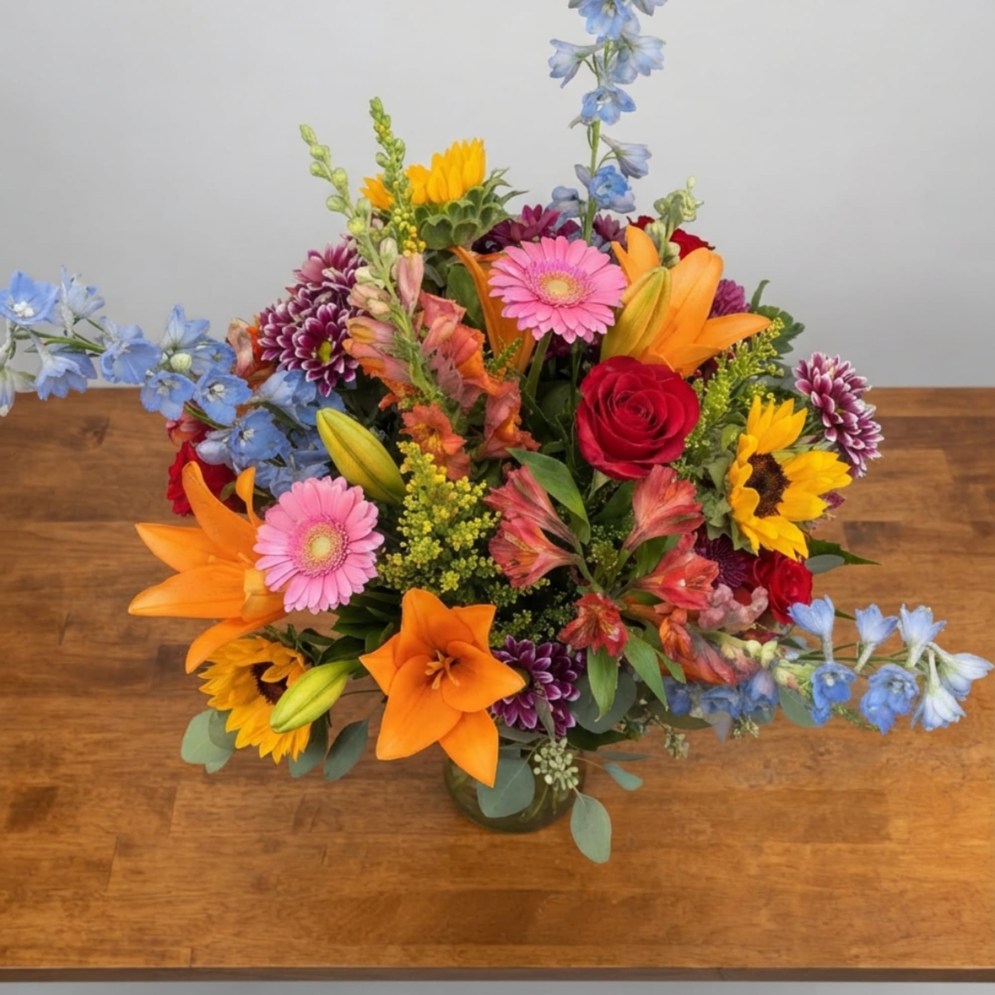 Colorful mixed bouquet with lilies, roses, gerbera daisies, and sunflowers in a glass vase