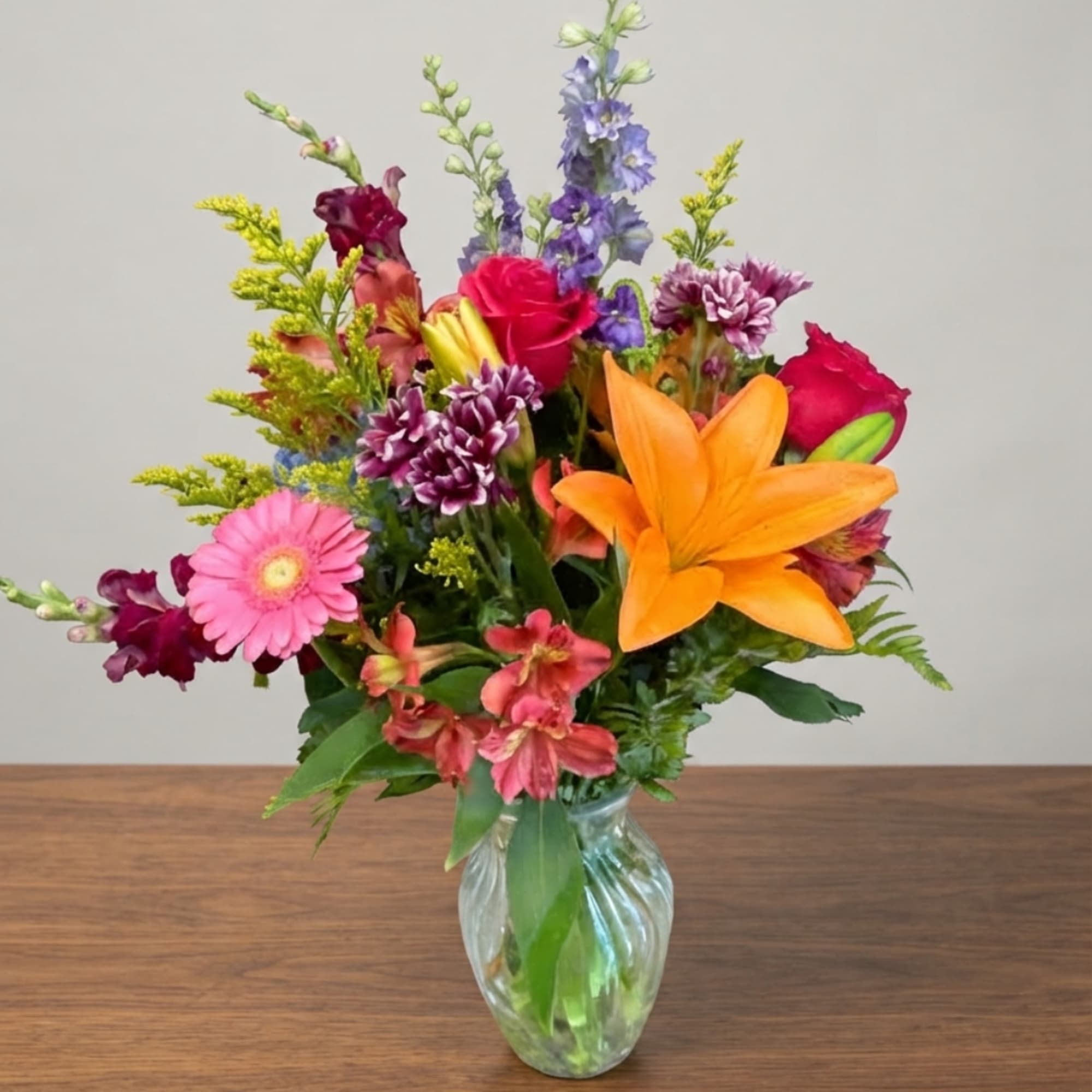 Mixed bouquet with lilies, roses, gerbera daisies, and purple blooms in a glass vase