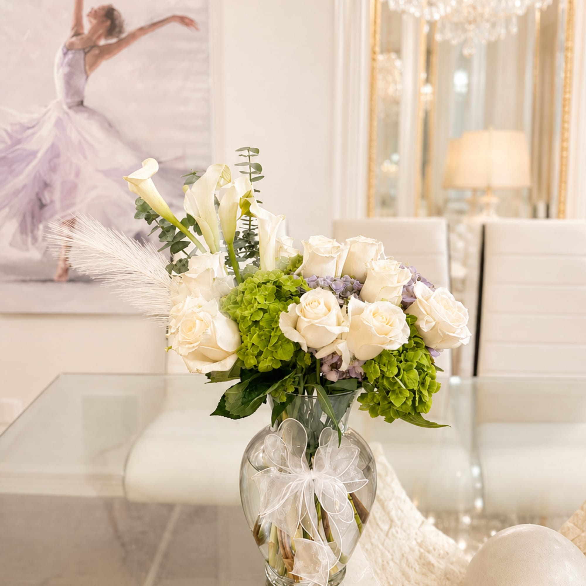 White roses and calla lilies in a glass vase with a ribbon bow