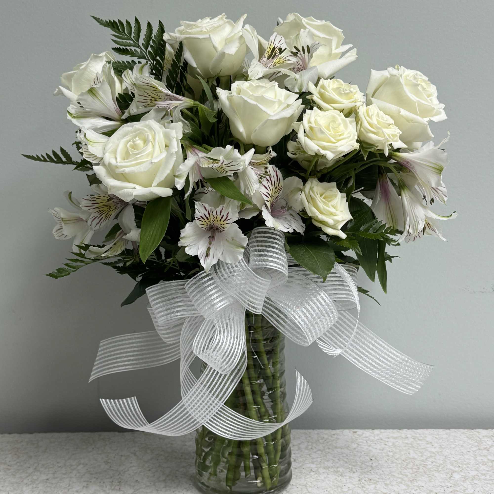 White rose bouquet in a glass vase with a sheer ribbon bow