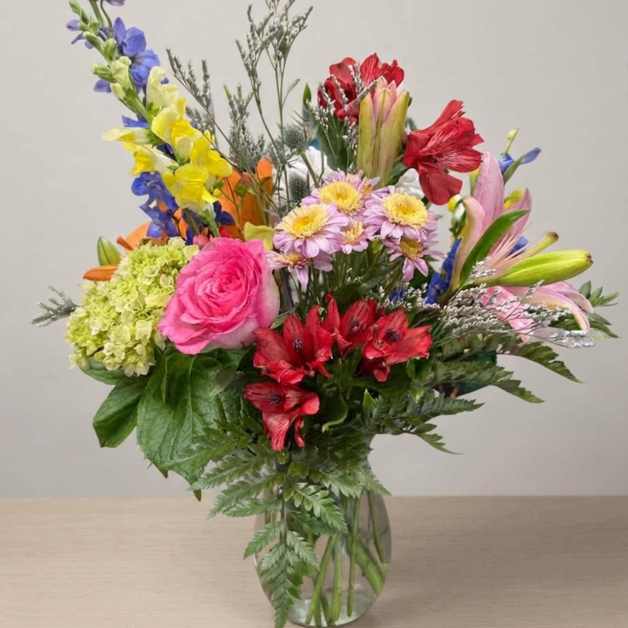 Colorful mixed bouquet in a clear glass vase with roses, lilies, and daisies