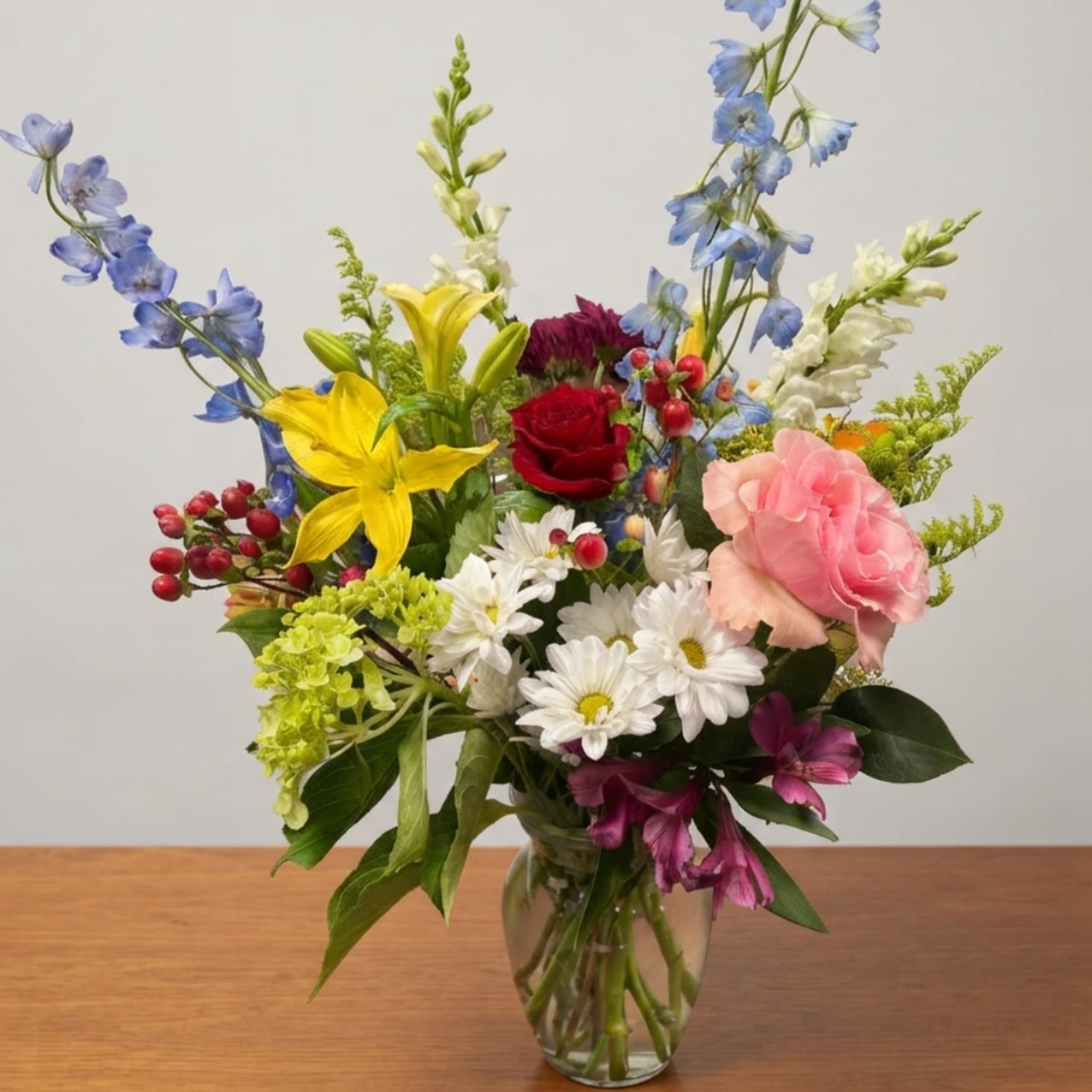 Mixed bouquet of lilies, roses, daisies, and delphinium in a glass vase