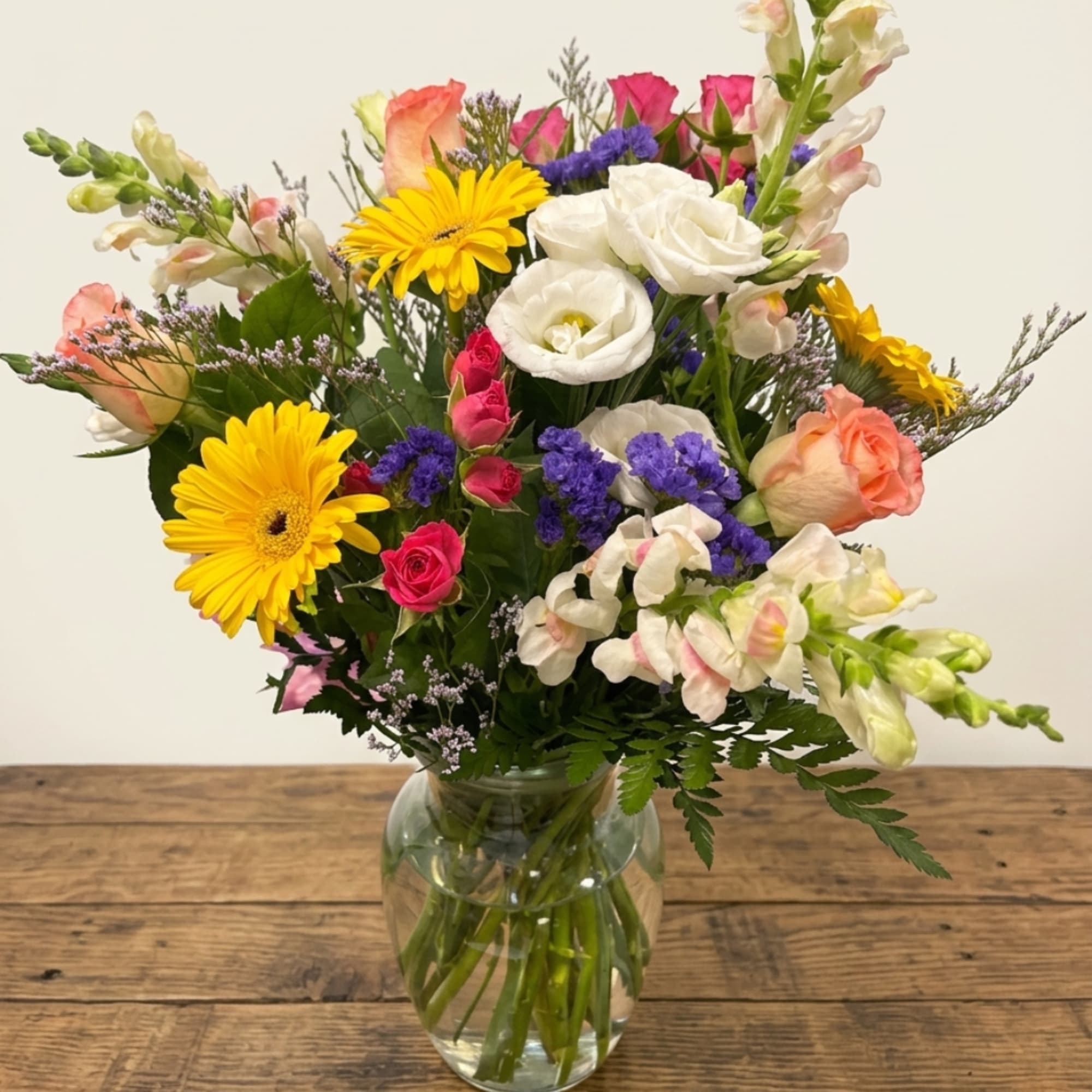 Mixed bouquet of yellow gerbera daisies, roses, and white blooms in a glass vase
