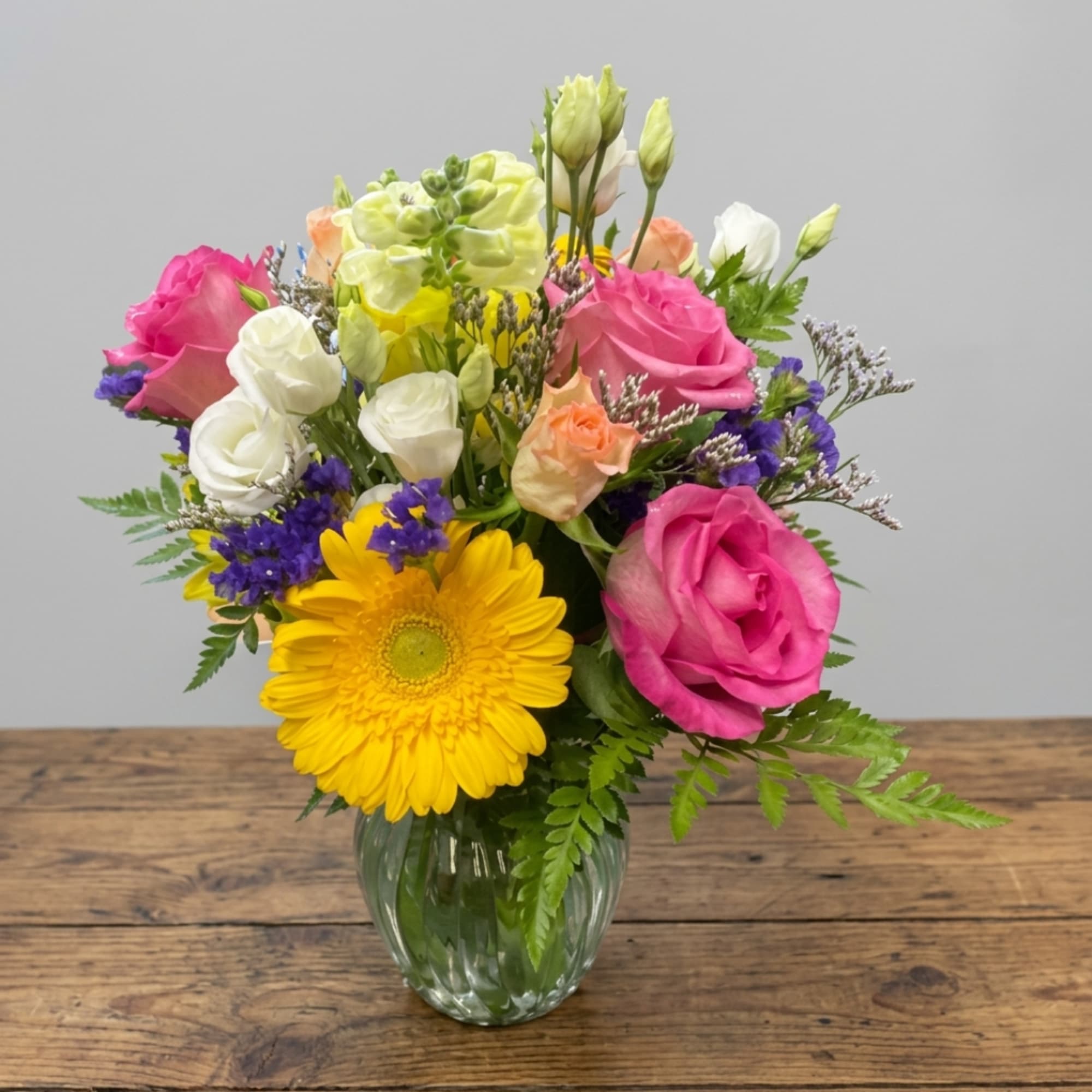 Mixed bouquet of roses, gerbera daisies, and lisianthus in a glass vase