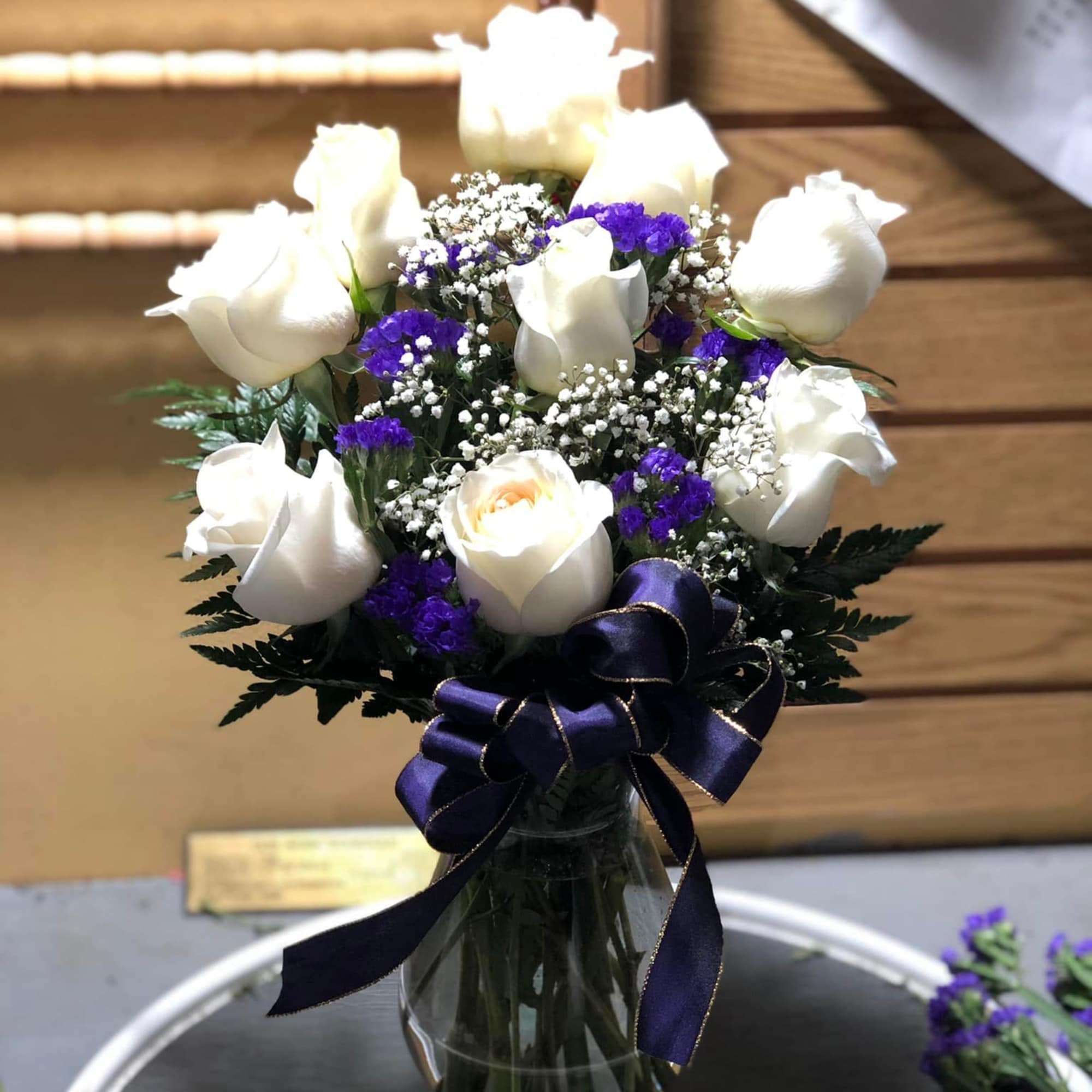 White roses and purple filler flowers in a glass vase with a ribbon