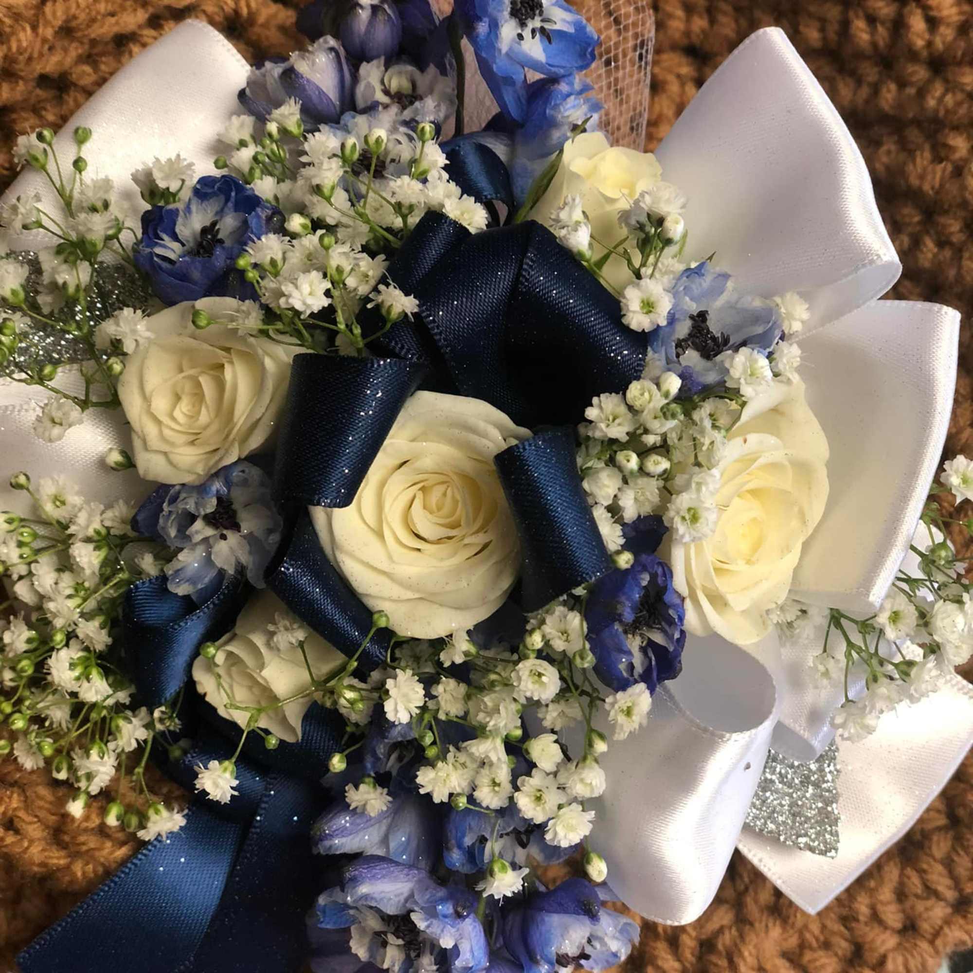 White roses with blue flowers and navy ribbon on a white bow