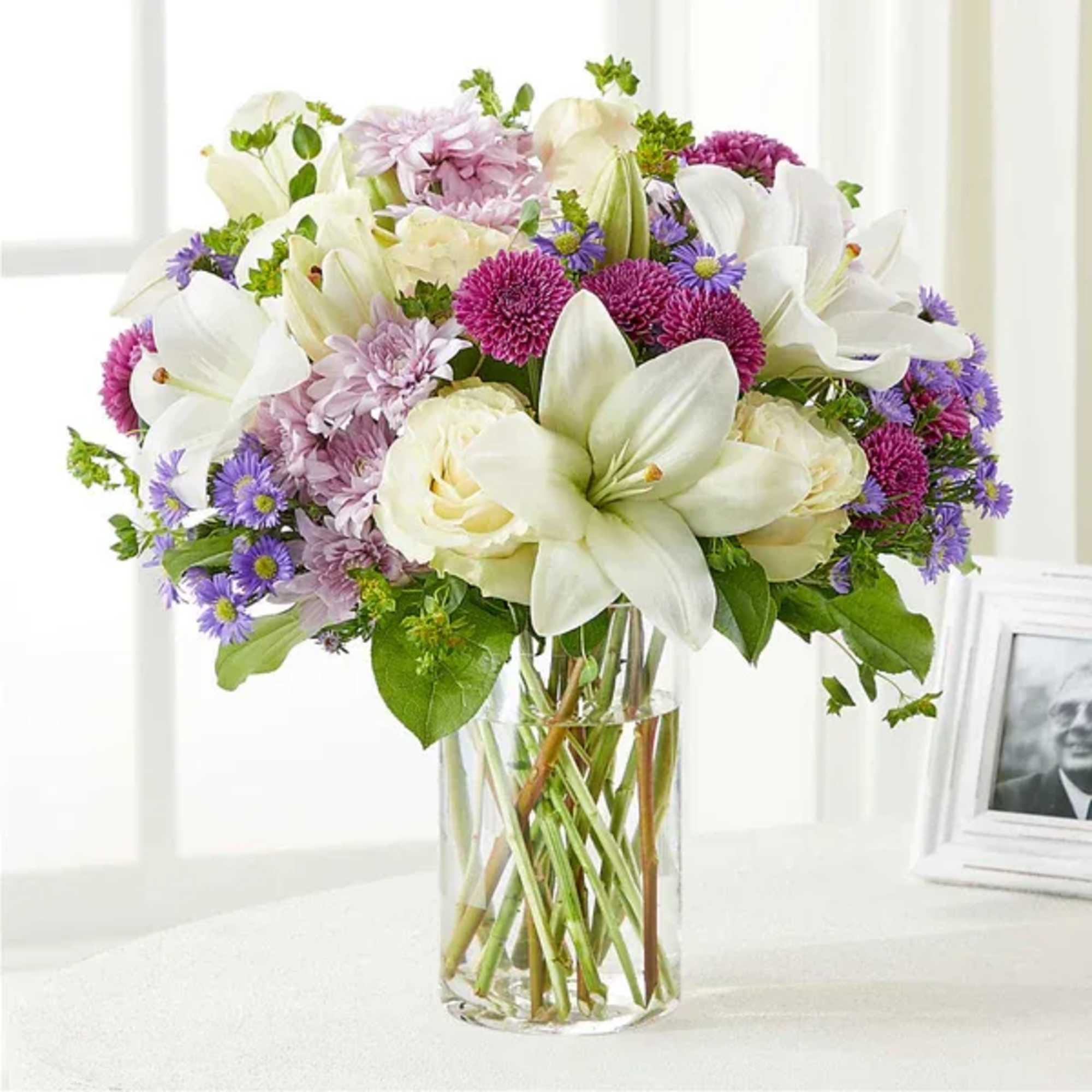 Bouquet of white lilies, roses, and purple daisies in a clear glass vase