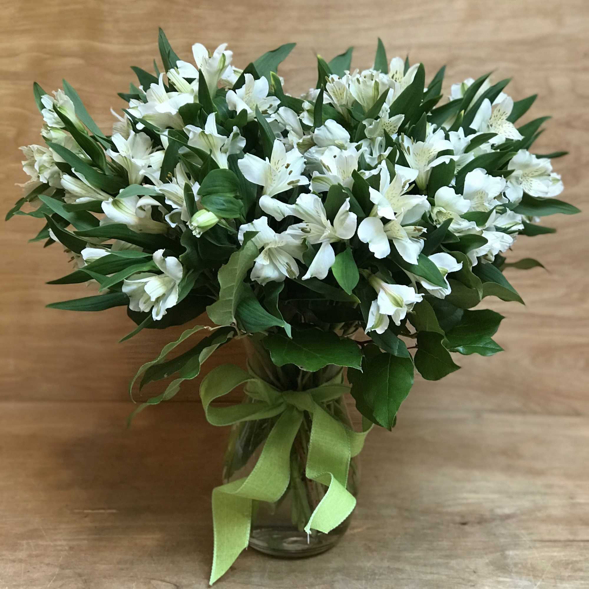 White alstroemeria bouquet in a glass vase with a green ribbon