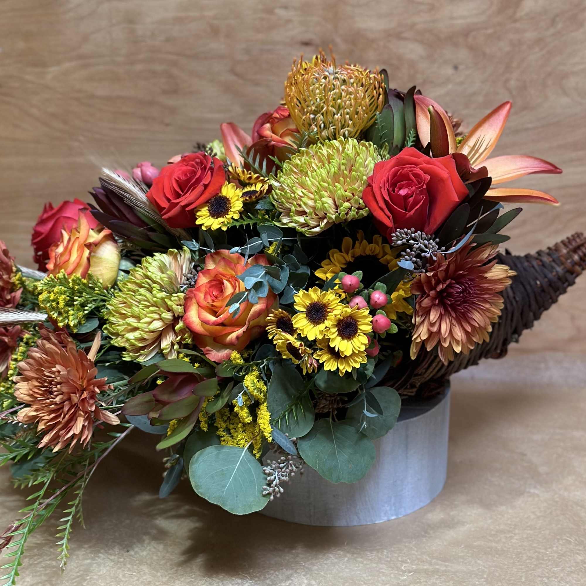Mixed bouquet with red roses, chrysanthemums, and tropical blooms in a round container