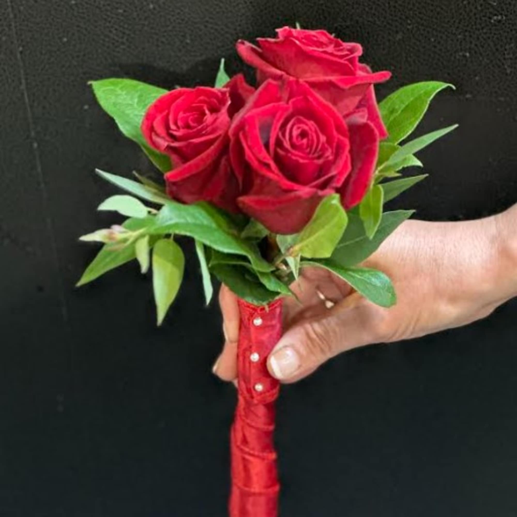 Small bouquet of red roses with green leaves and a red wrapped handle