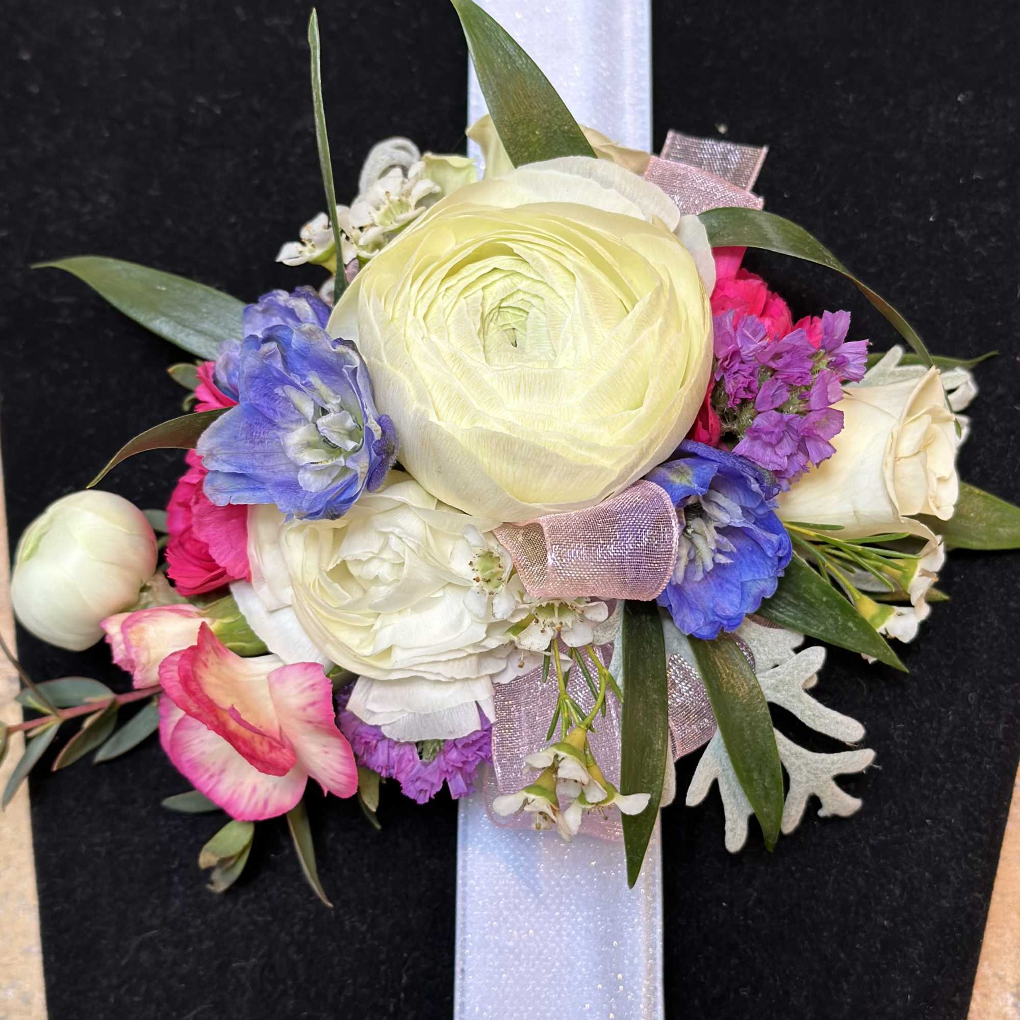 Floral wrist corsage with cream, pink, and purple blooms on a white band