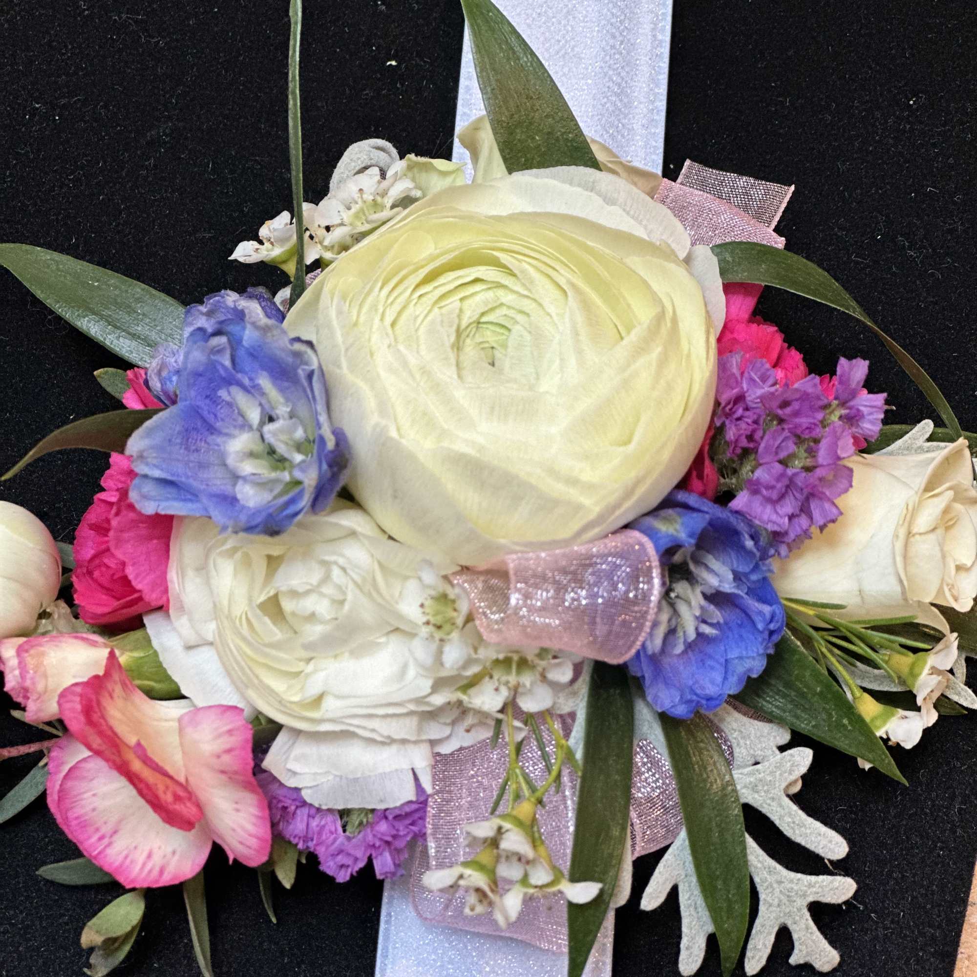 Floral corsage with cream, pink, and blue blooms on a white ribbon
