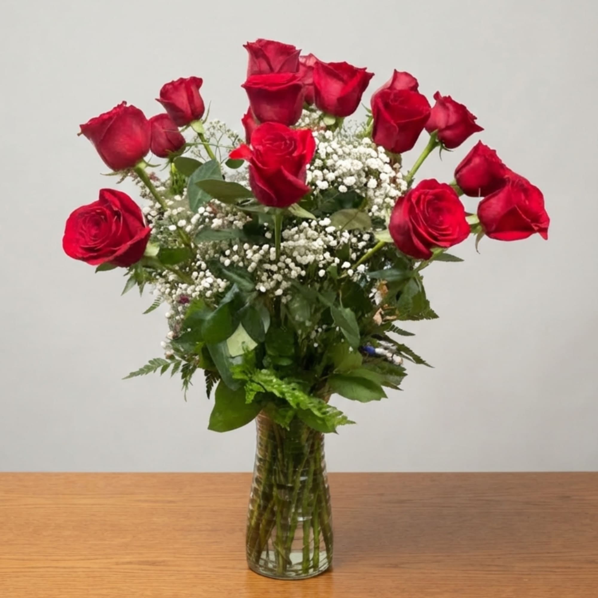 Red roses arranged in a clear glass vase with baby's breath