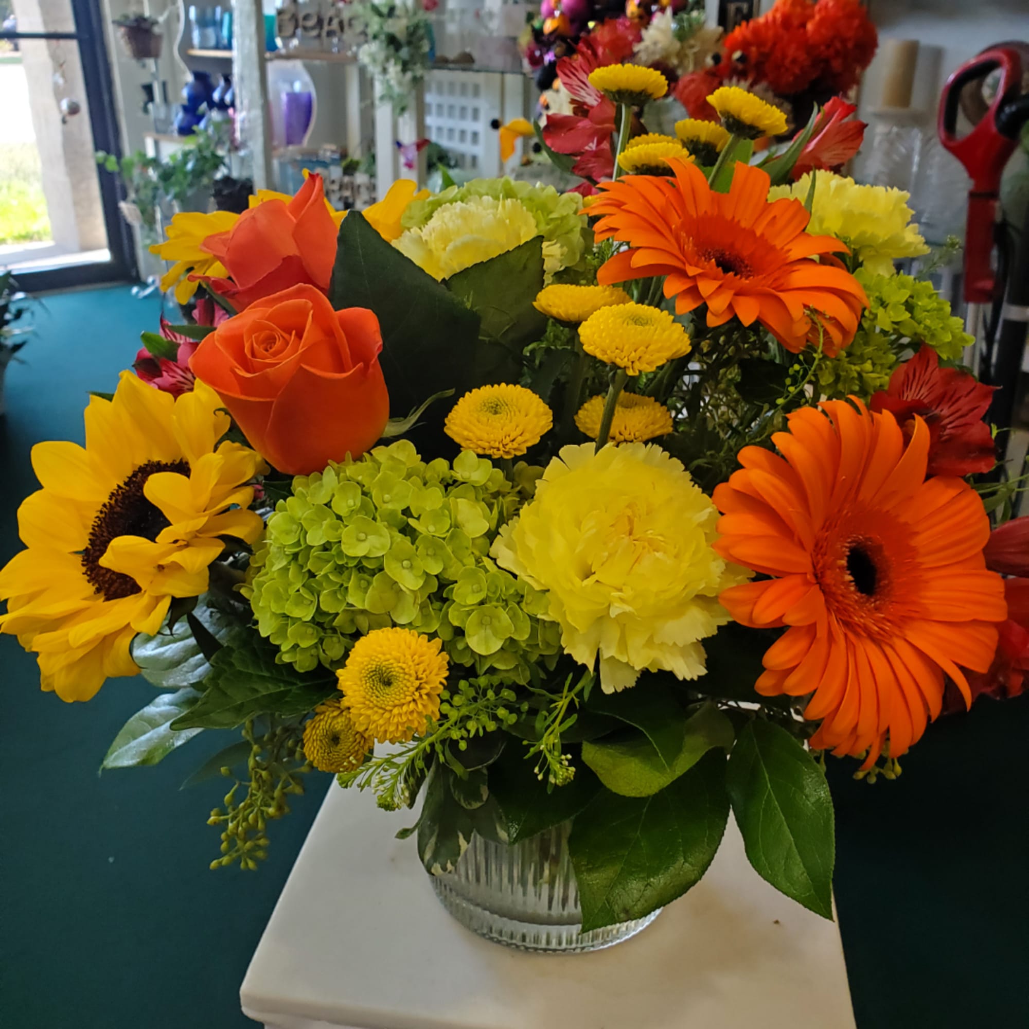 Bright mixed flower arrangement in a clear glass vase with orange, yellow, and green blooms