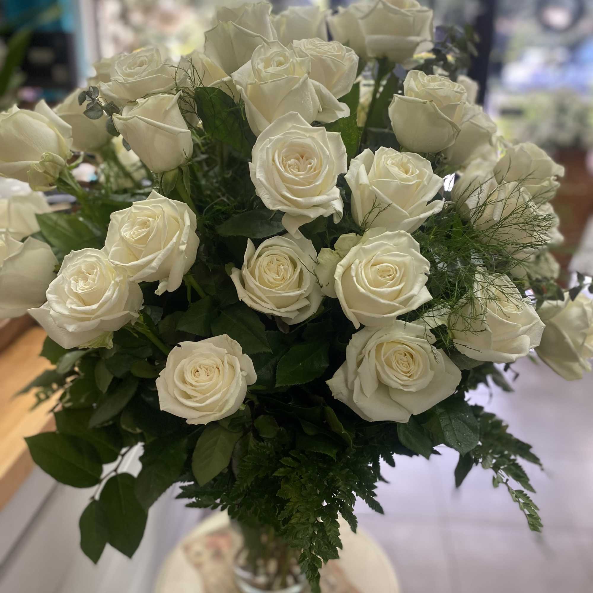 Over 2 dozen creamy white roses with lush green foliage in a