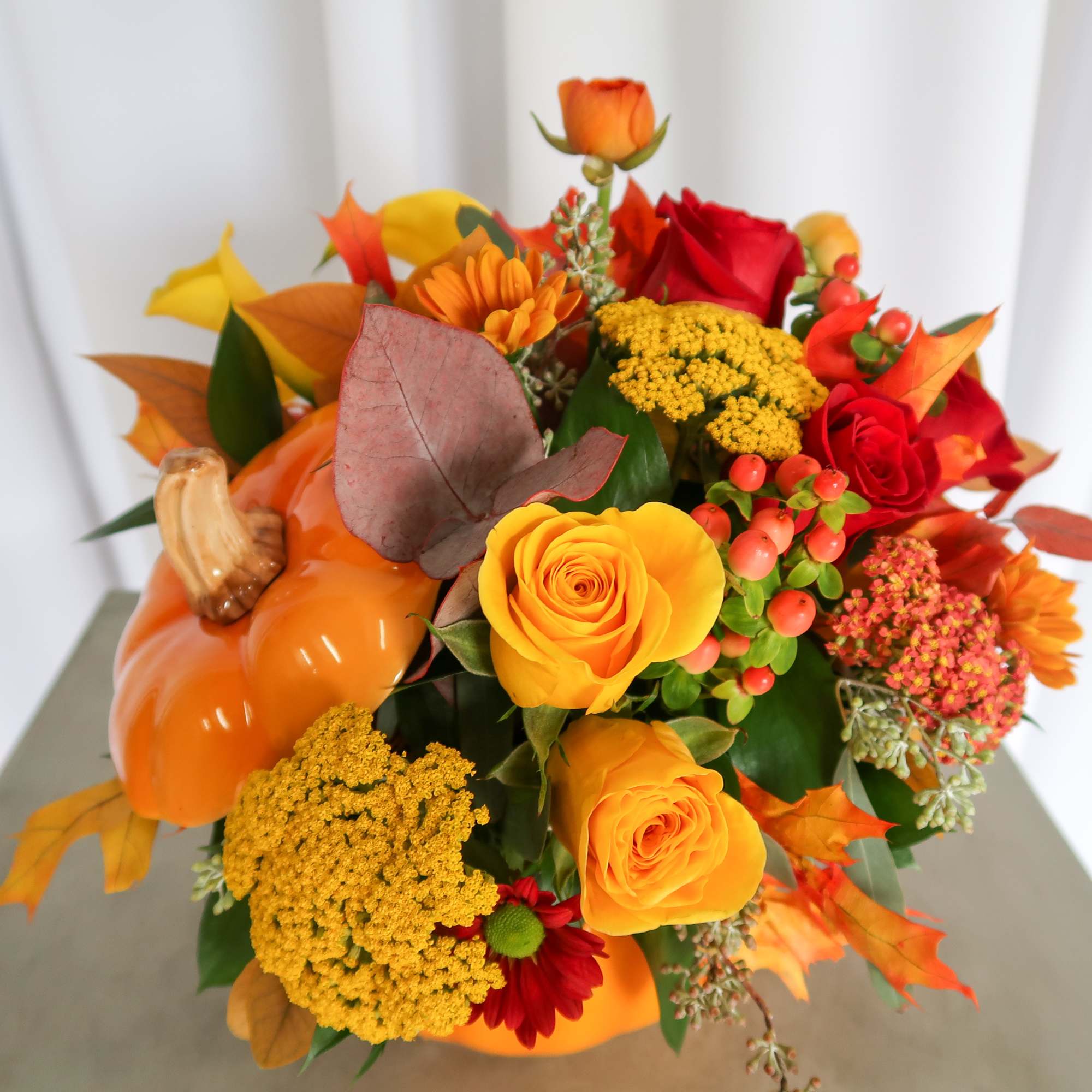 Autumn floral arrangement in an orange pumpkin container with roses and mixed blooms