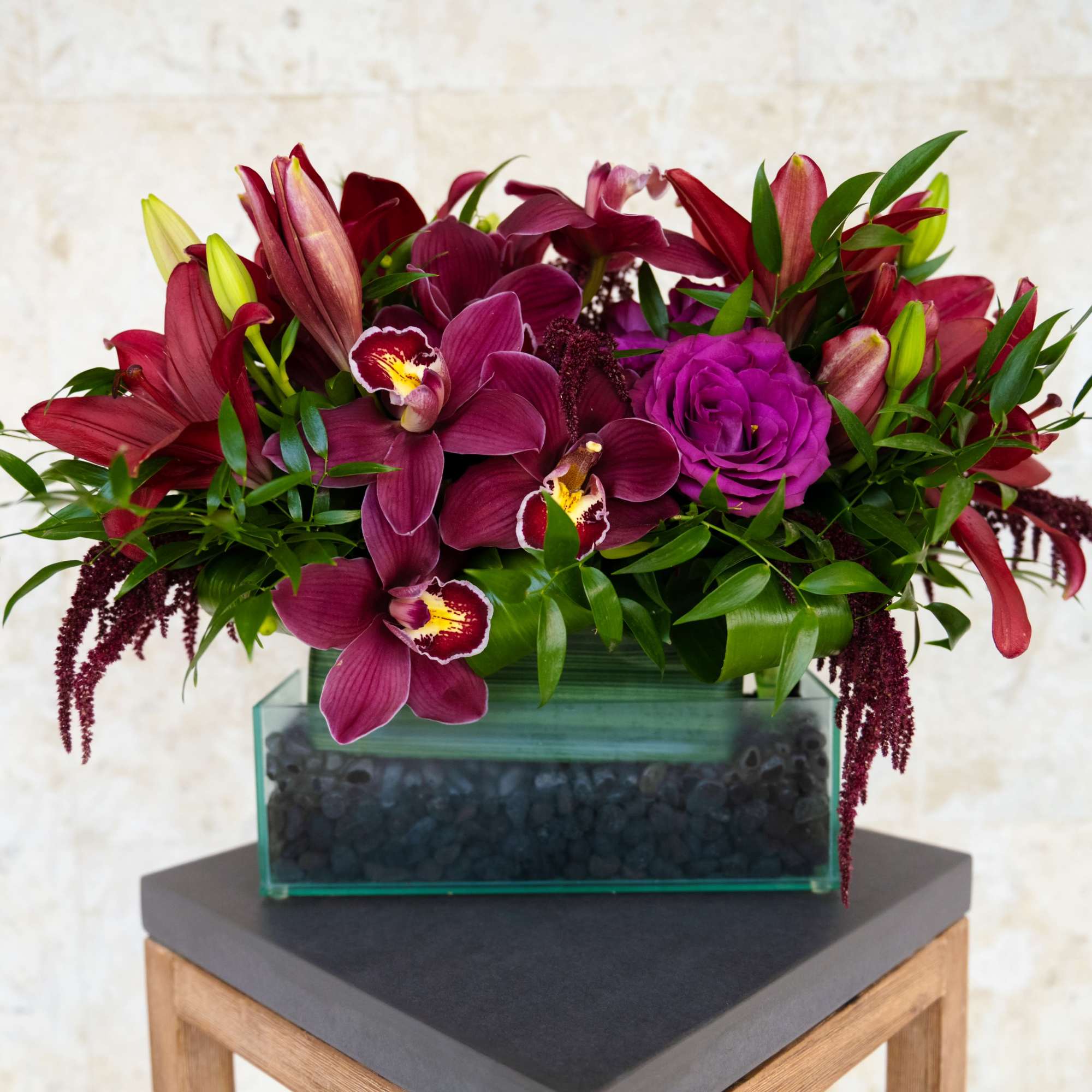 Magenta floral arrangement in a rectangular glass vase on a wooden stand