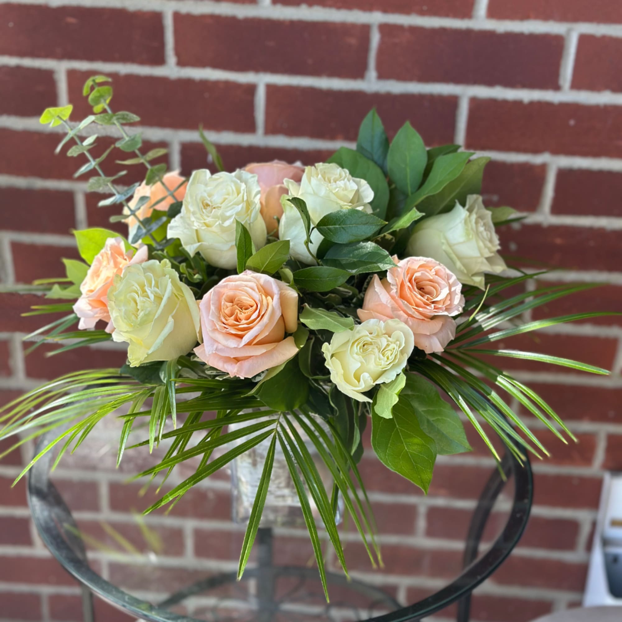 Bouquet of peach and cream roses with greenery in a clear vase