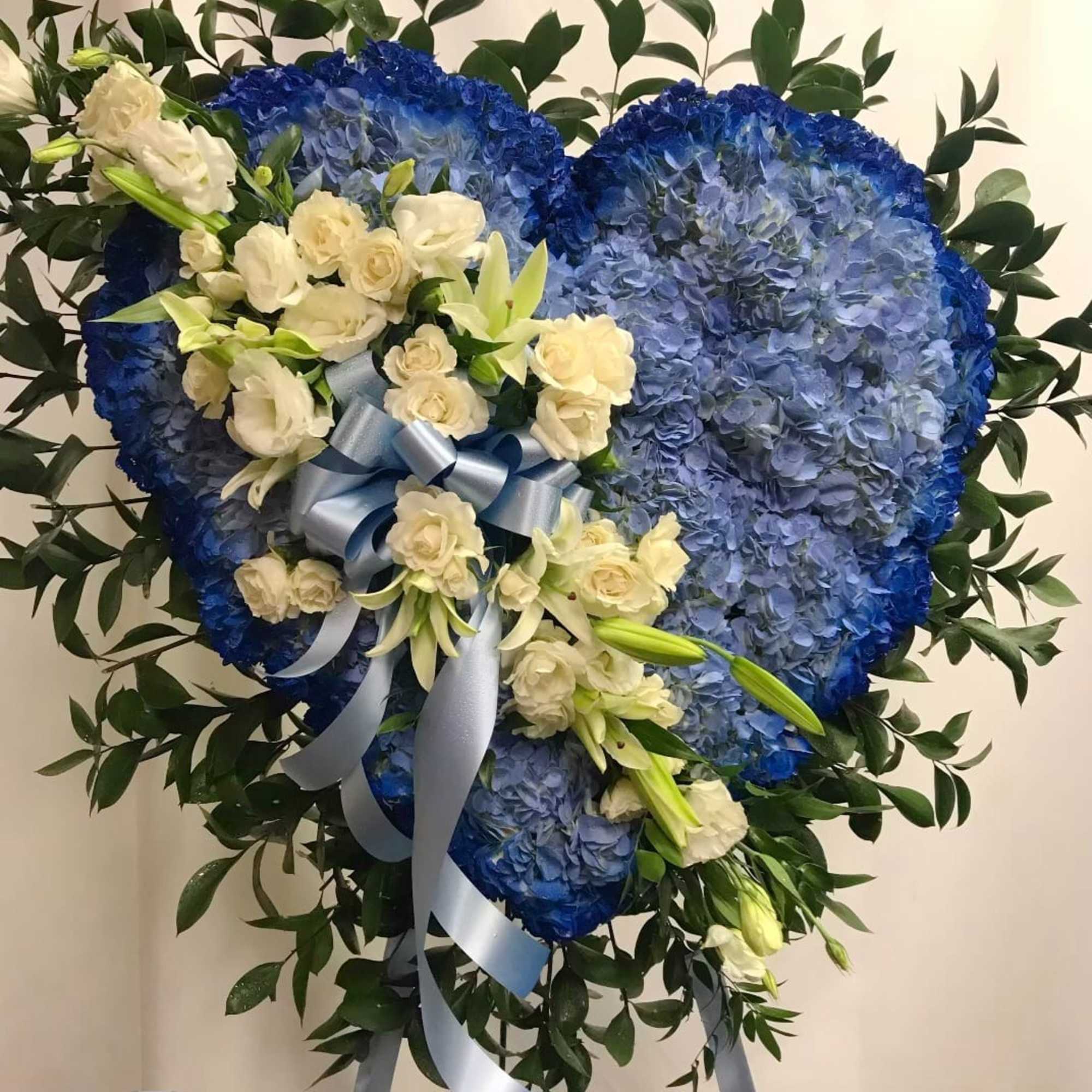Heart-shaped blue floral tribute with white roses and lilies
