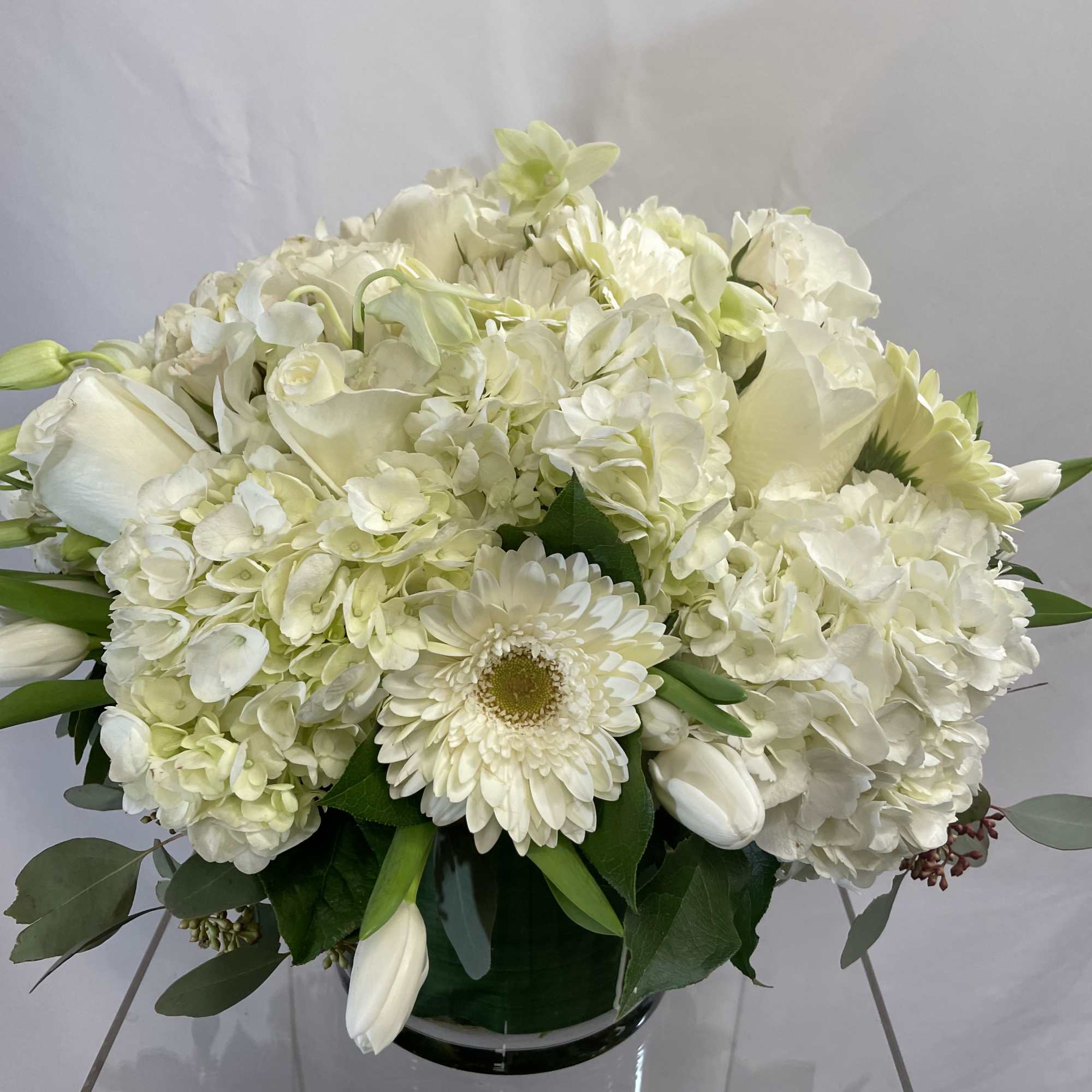 White floral arrangement with hydrangeas, roses, and a gerbera daisy in a glass vase