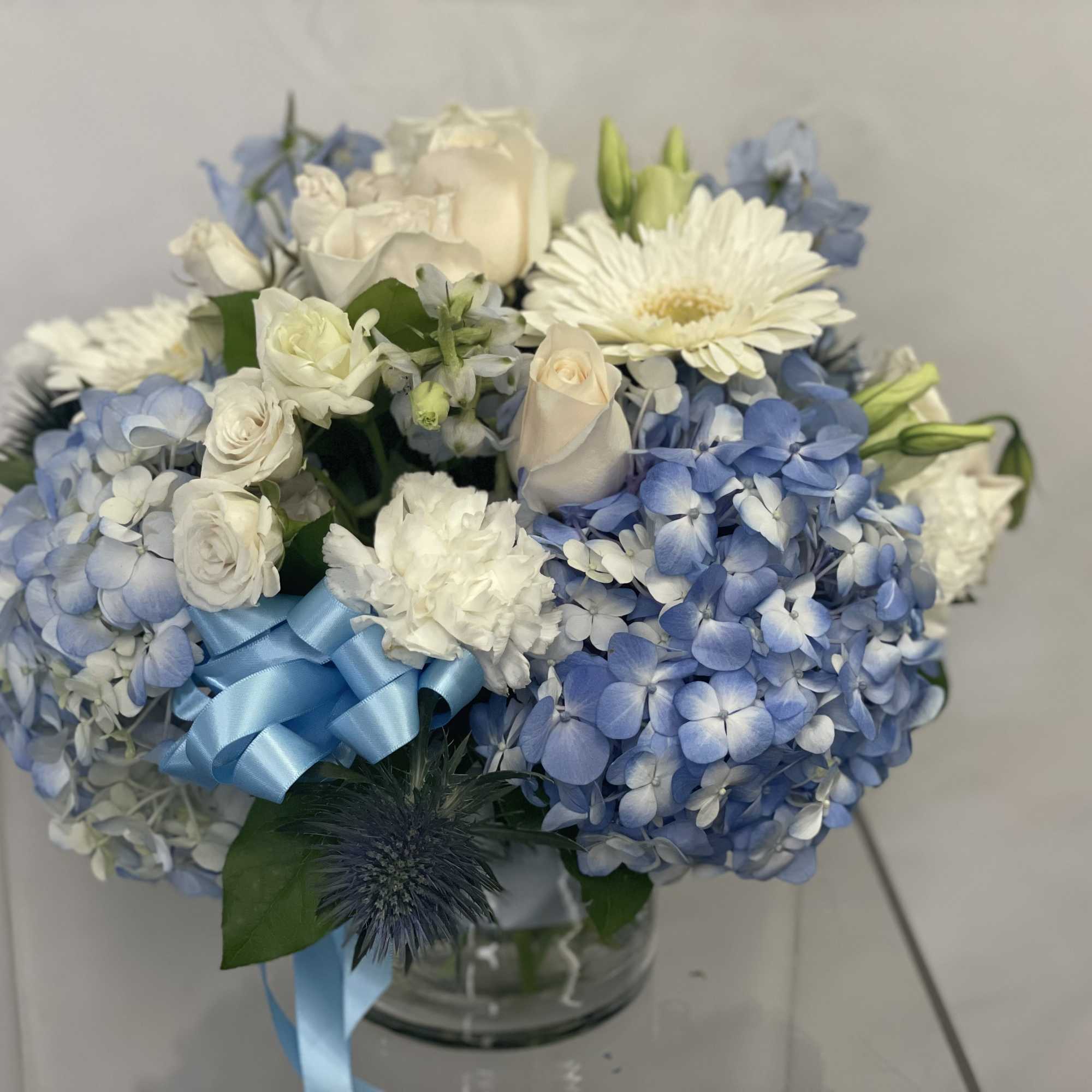 Blue and white floral arrangement in a glass vase with a blue ribbon