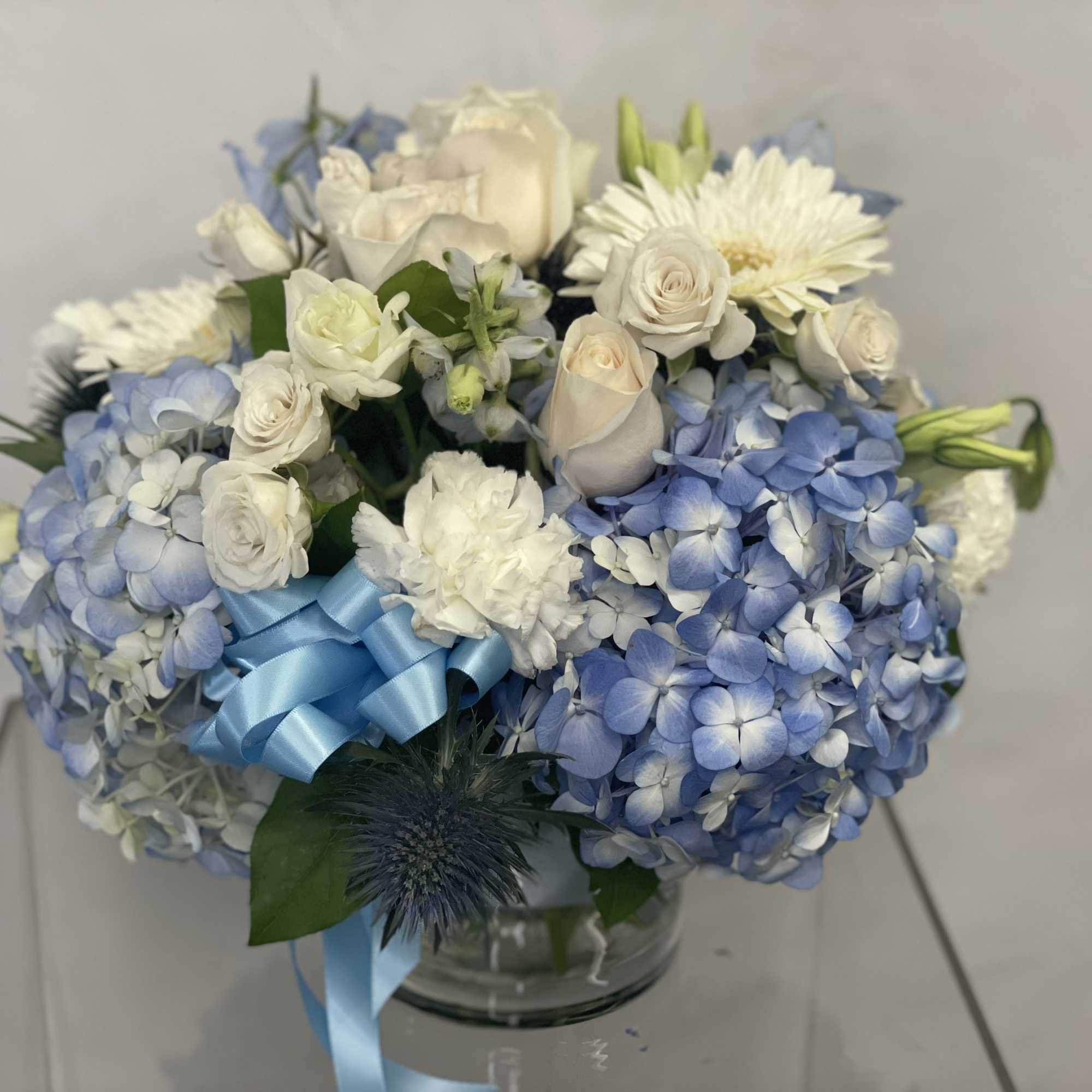 Blue and white bouquet of hydrangeas and roses in a glass vase with a blue ribbon