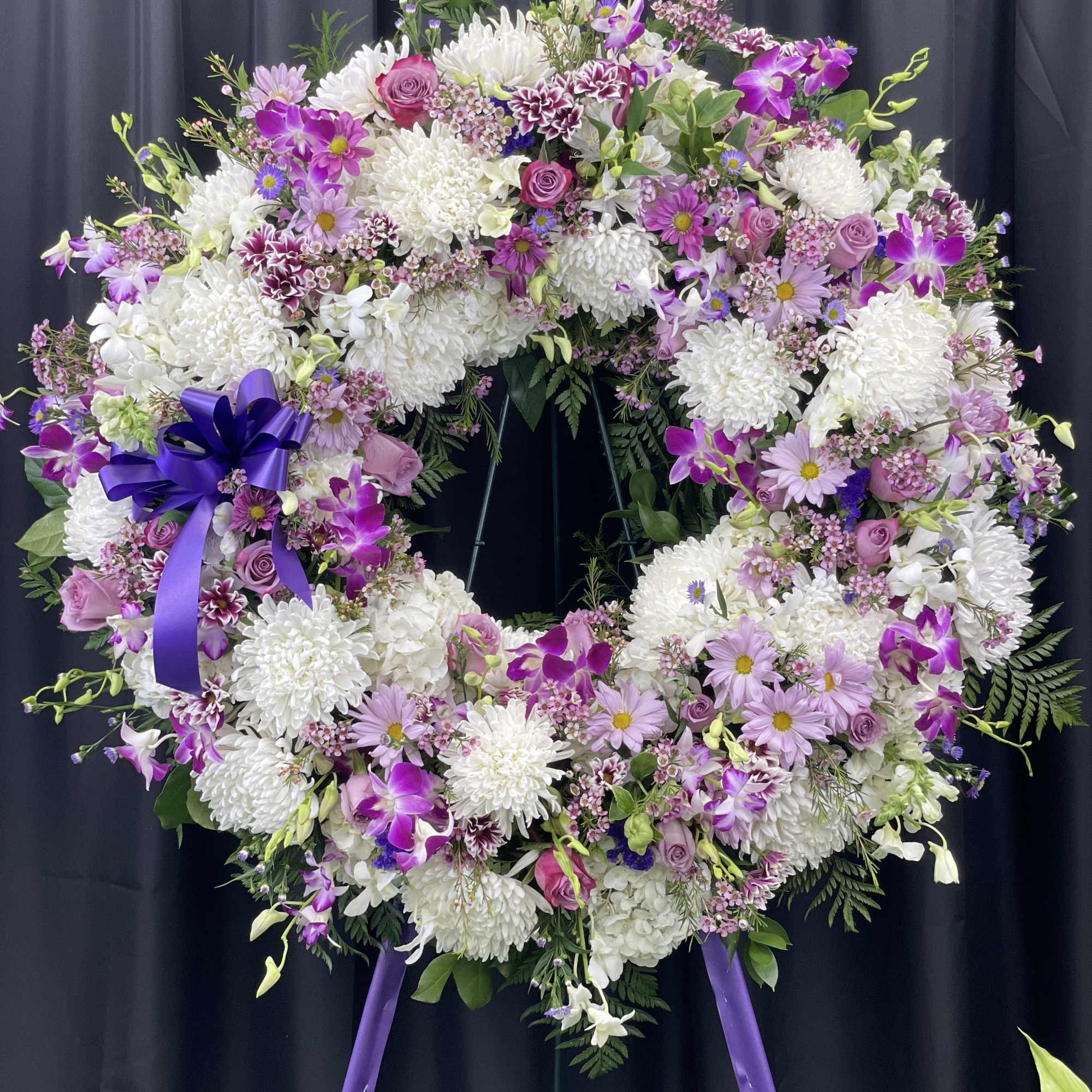 Large purple and white floral wreath on a stand with a ribbon bow