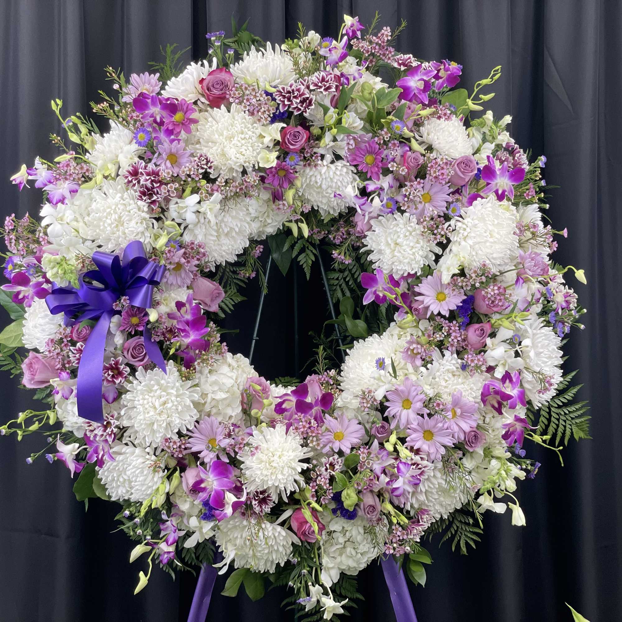 Large floral wreath with white and purple flowers on a dark stand